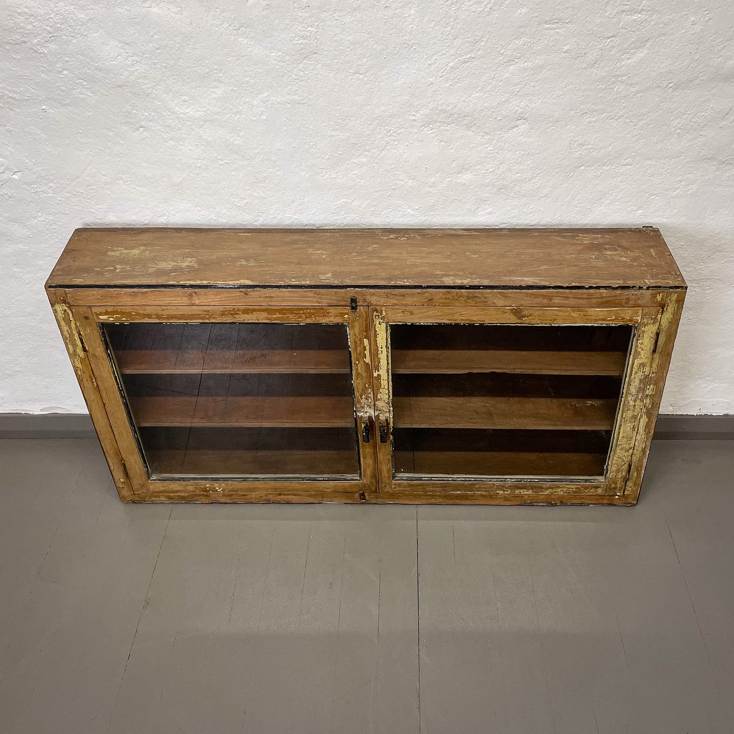 Wooden cabinet with glass doors on a plain floor and wall background