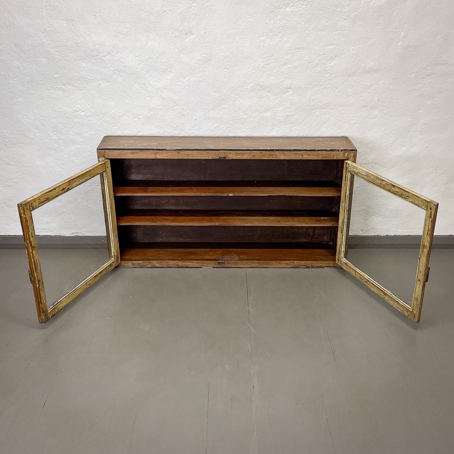 Wooden cabinet with glass doors on a plain floor and wall background