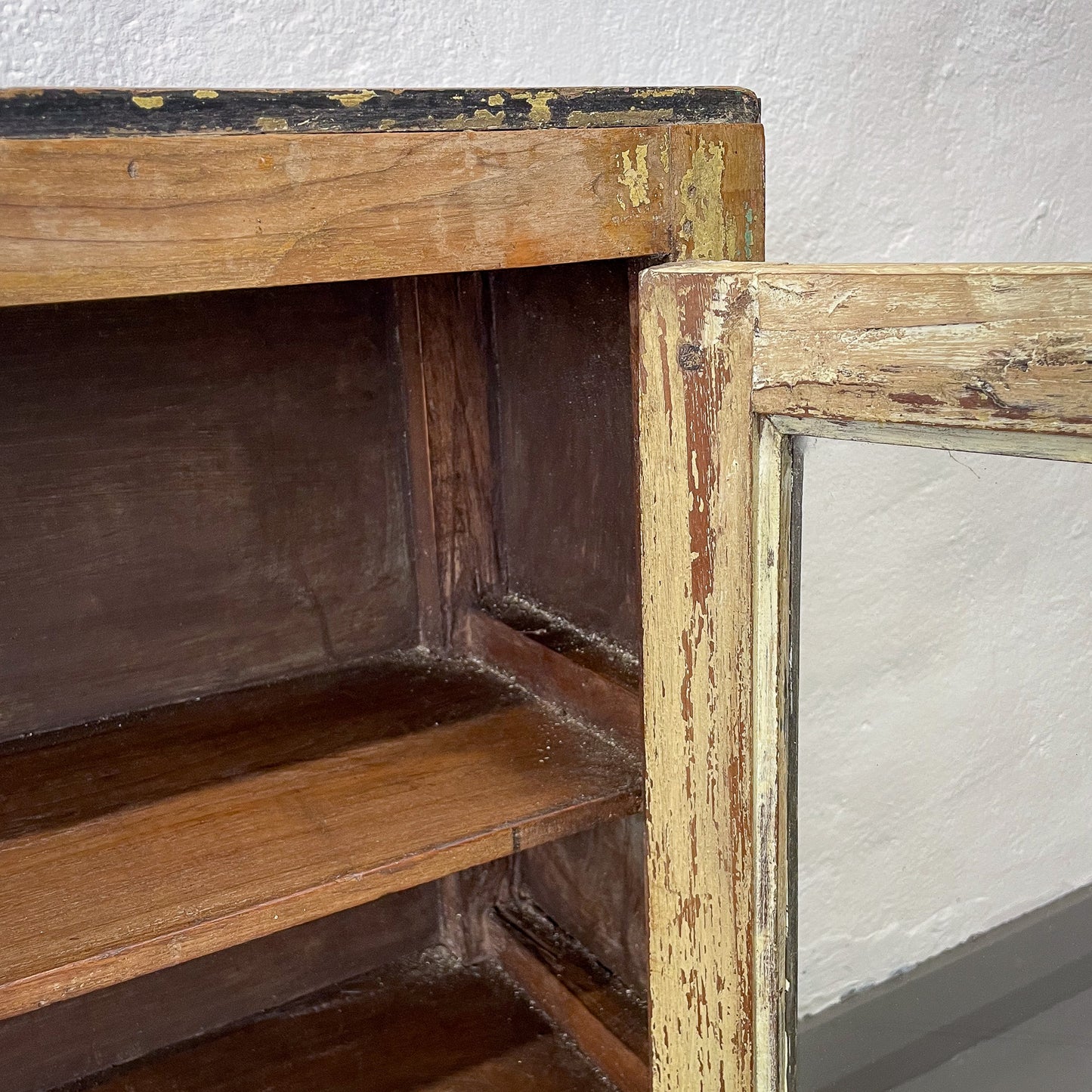 Old wooden shelf with peeling paint against a white wall