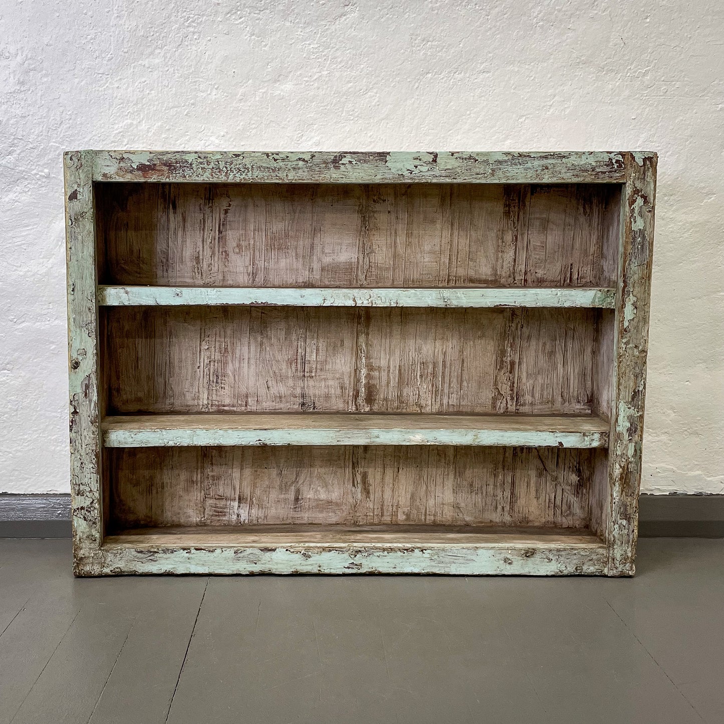 Wooden shelf with a weathered finish against a white wall.