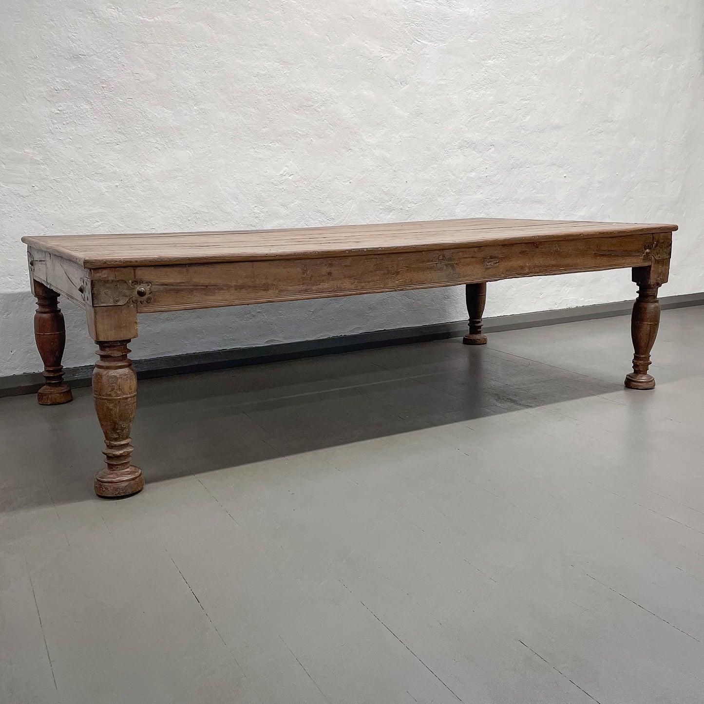 Wooden table with turned legs on a gray floor against a textured white wall