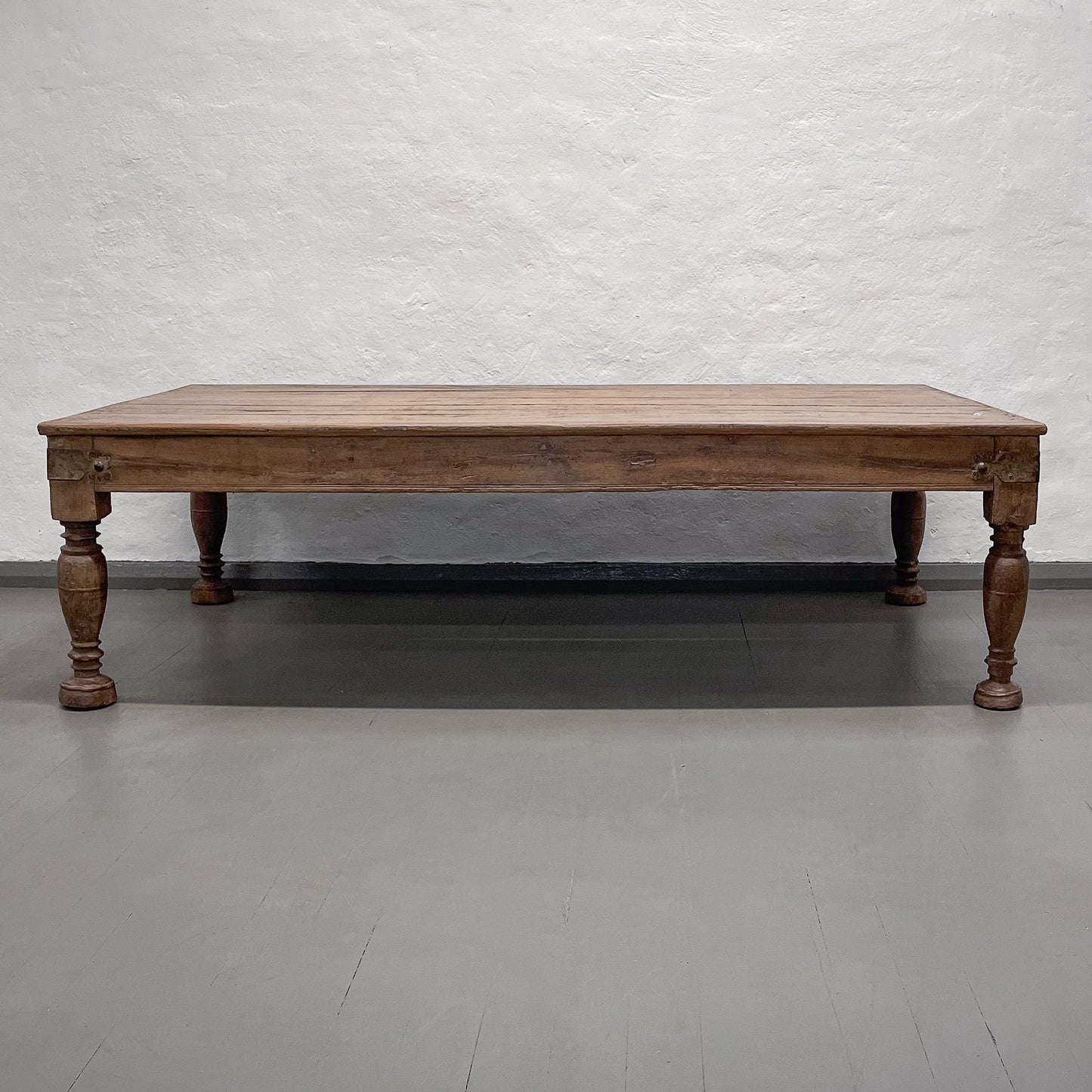 Wooden table with turned legs on a gray floor against a textured white wall