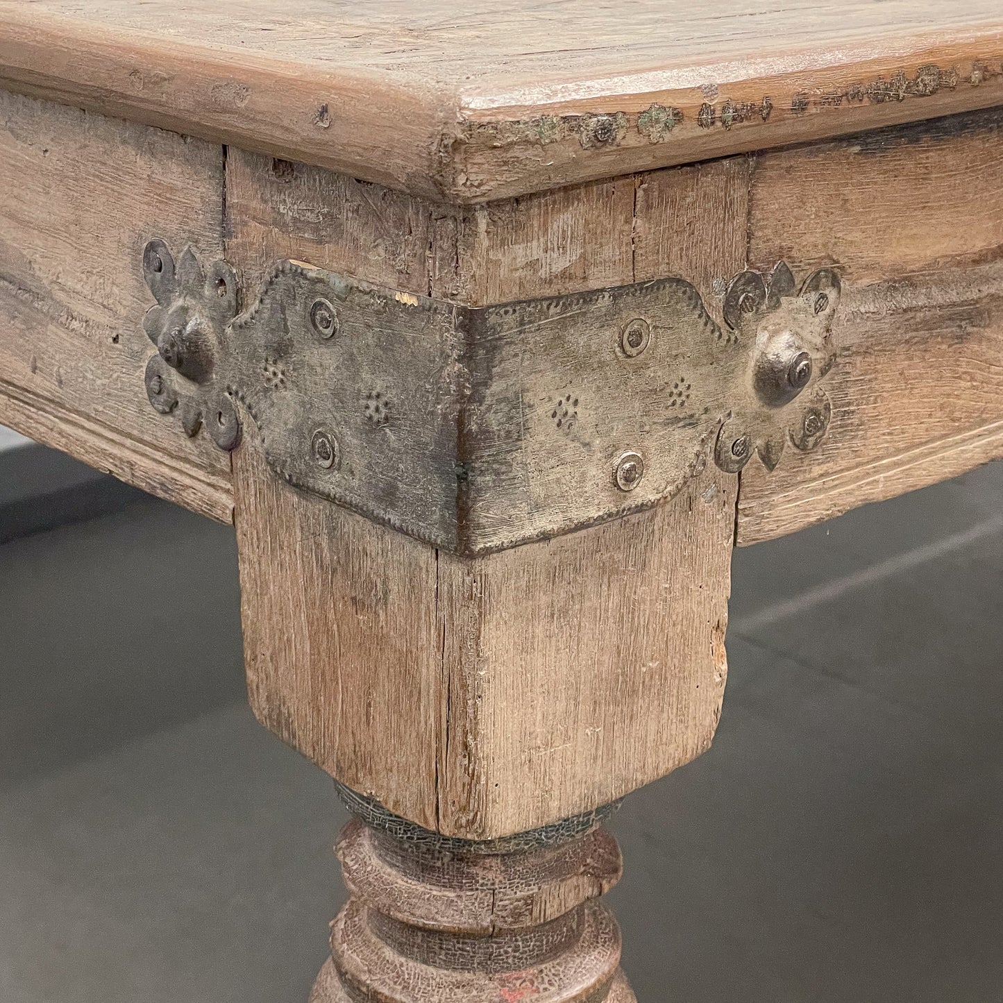 Close-up of a wooden table with decorative metal brackets on a gray background