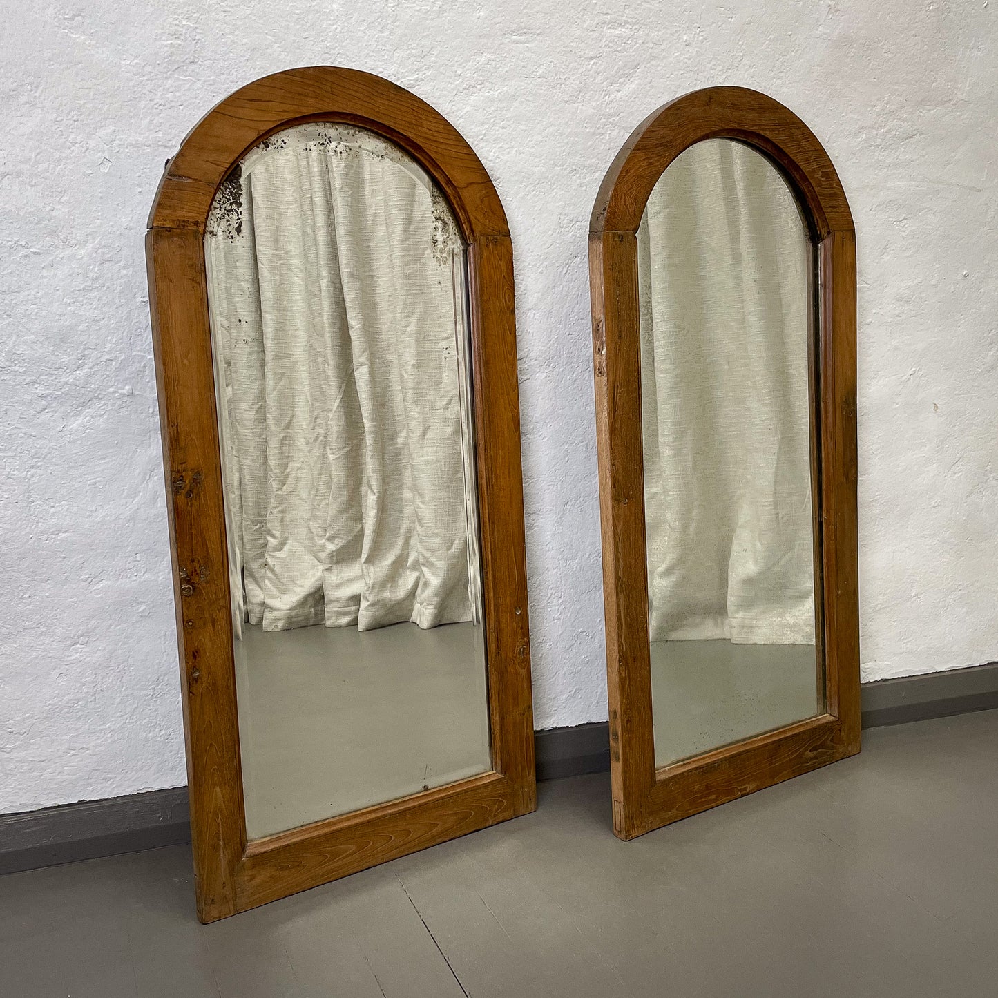 Two wooden-framed mirrors against a white textured wall.