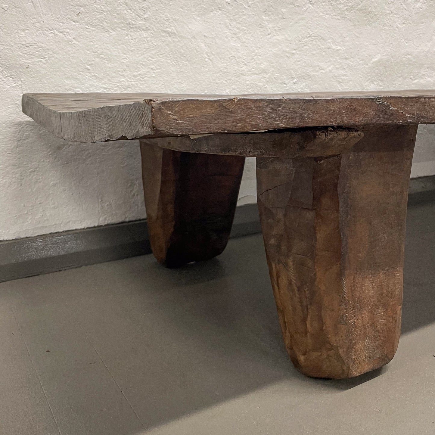 Wooden bench with natural finish against a textured white wall.