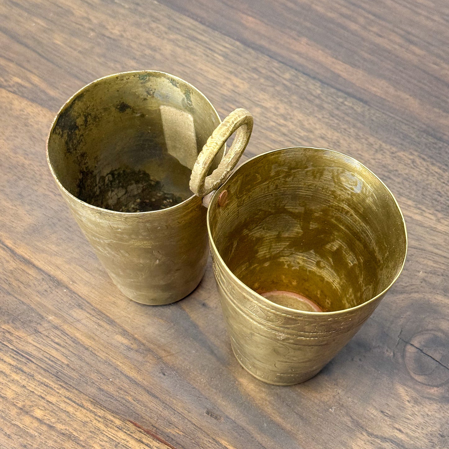 Two brass cups on a wooden surface
