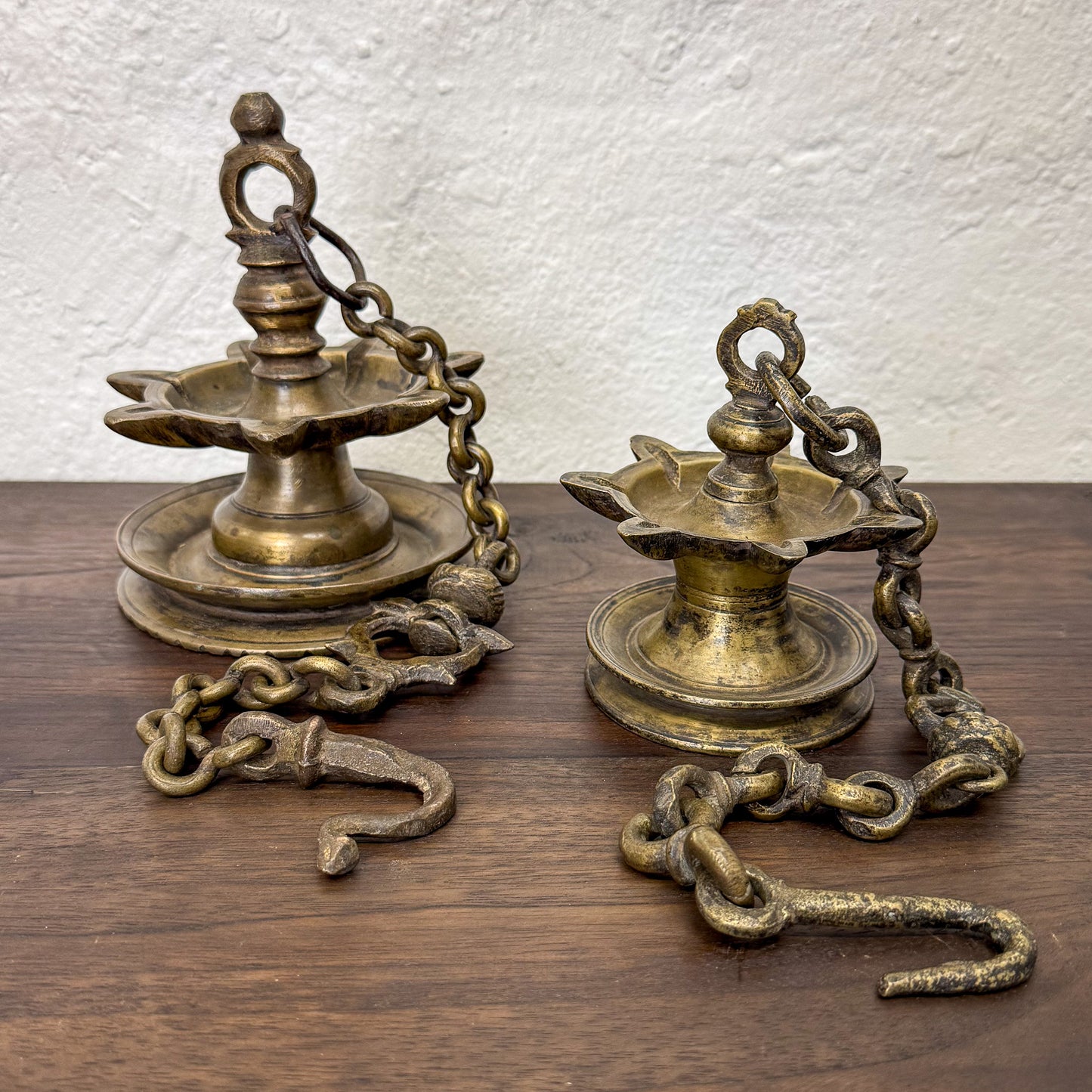 Two brass oil lamps with chains on a wooden surface and white textured wall background
