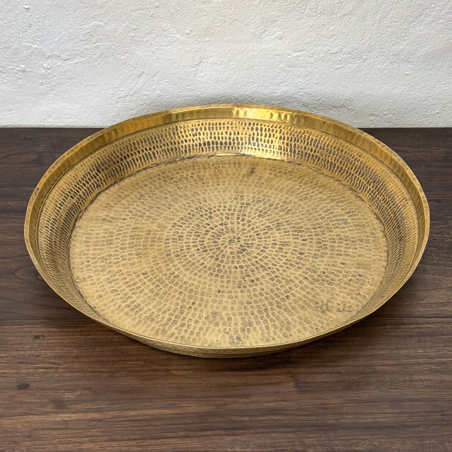 Gold decorative tray on a wooden surface with a white wall background