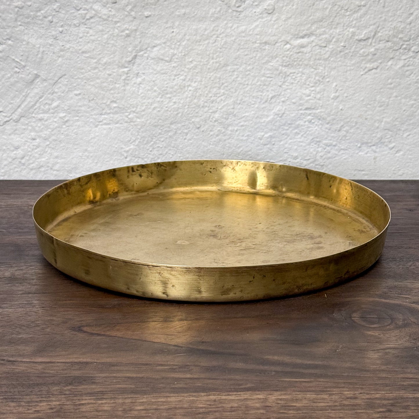Gold tray on a wooden surface with a white textured wall background