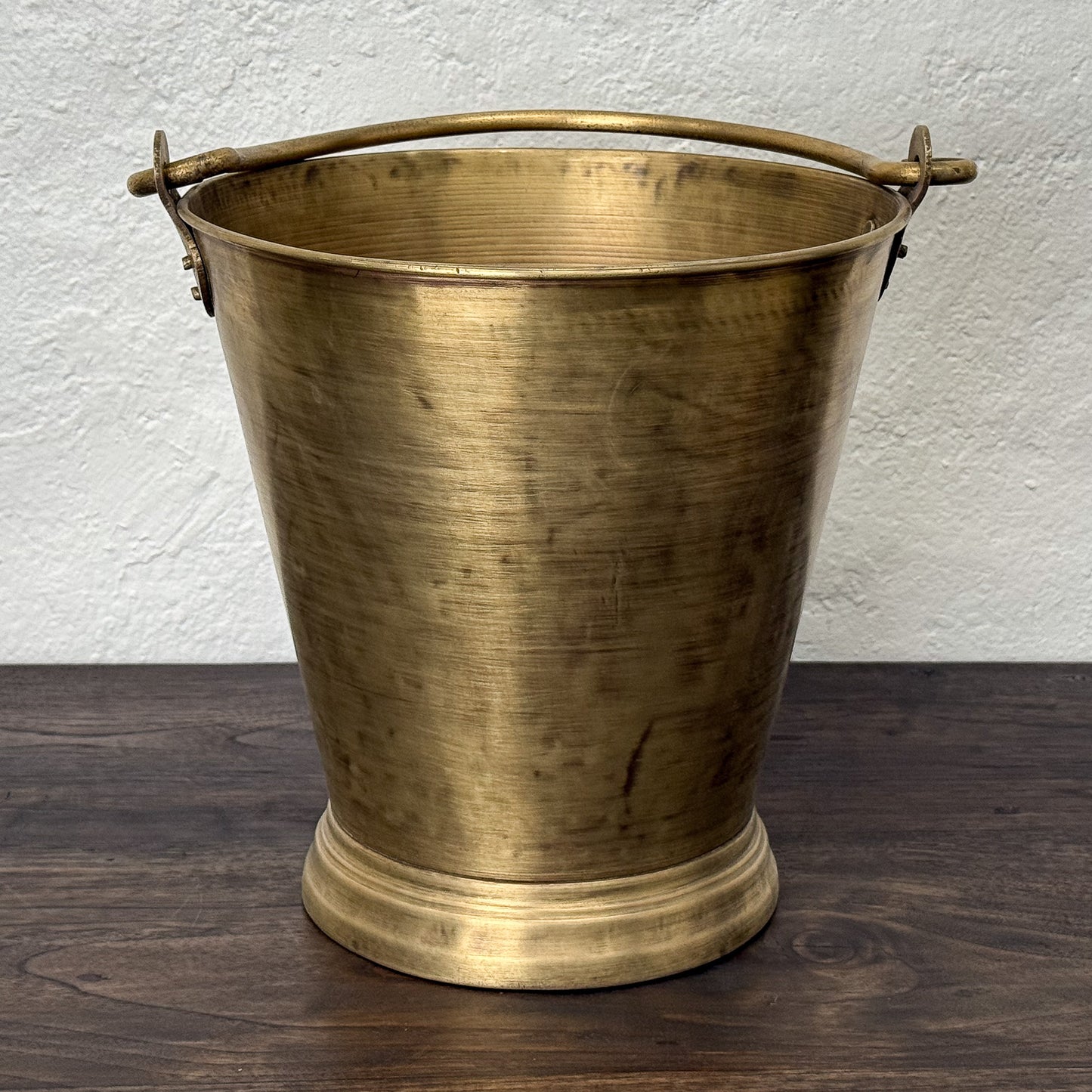 Brass bucket with handles on a wooden surface and white wall background