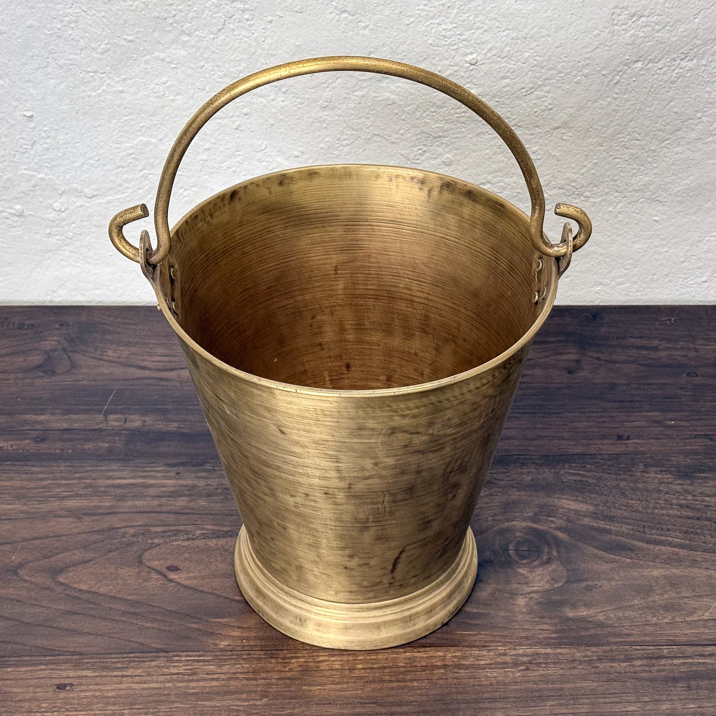 Brass bucket with handles on a wooden surface and white wall background