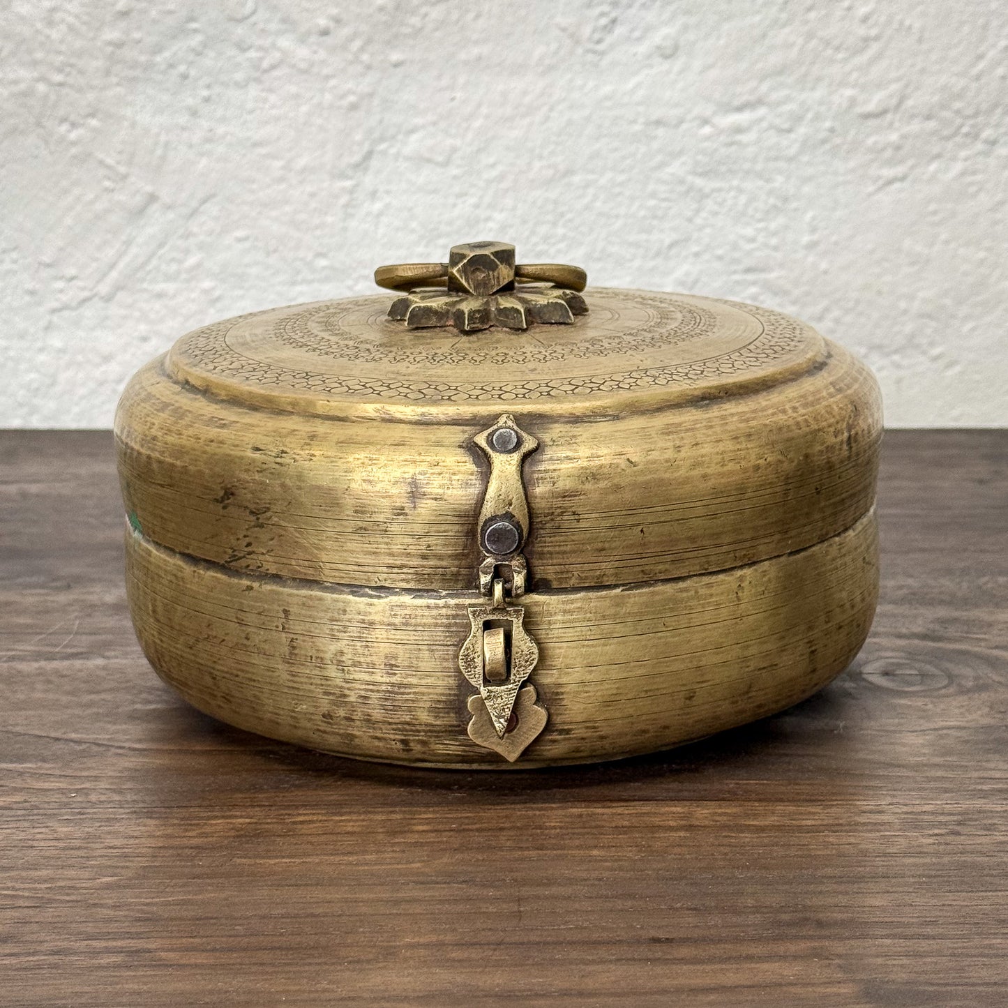 Brass decorative box with intricate designs on a wooden surface