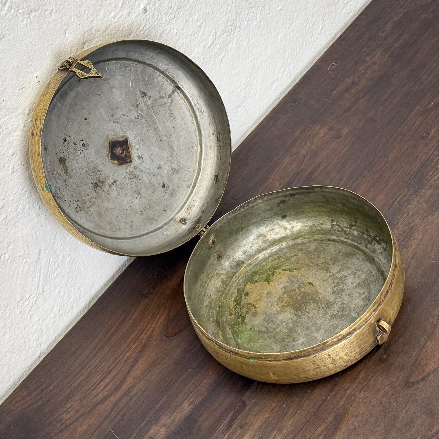 Two brass containers with a lid on a wooden surface