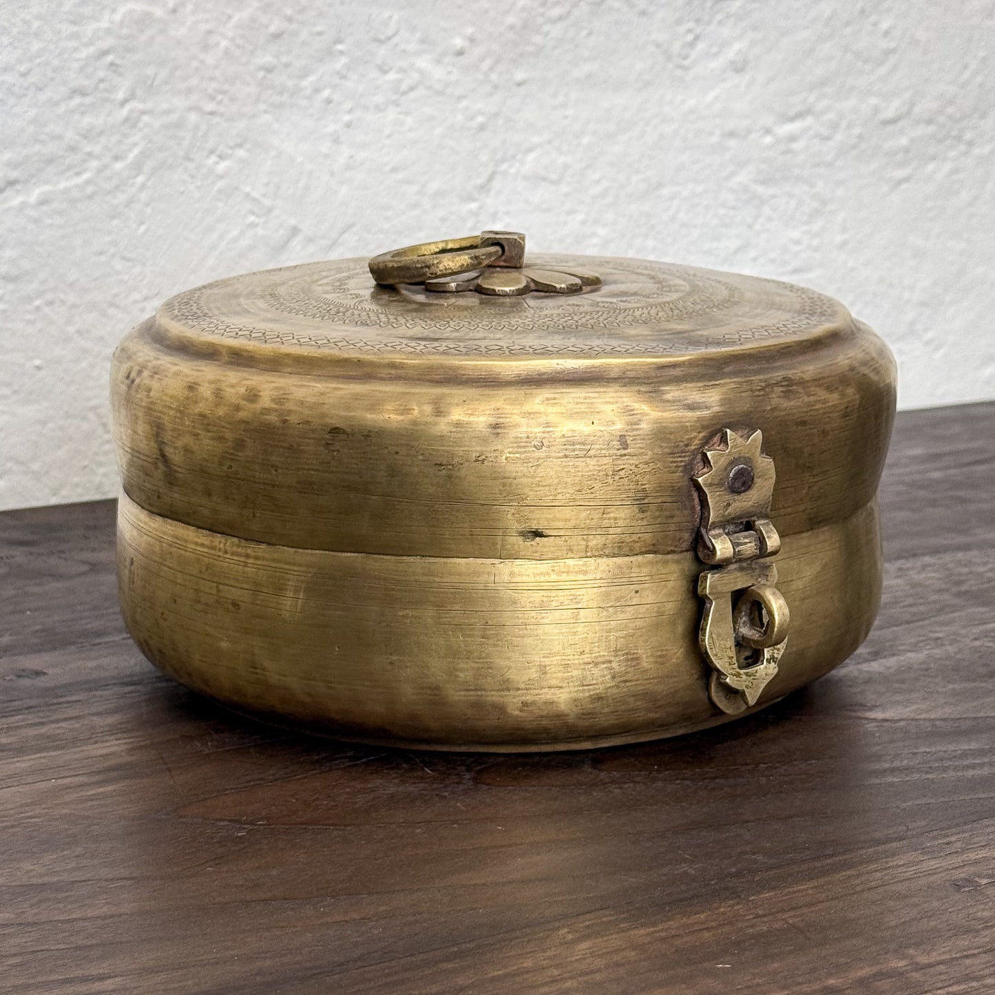 Brass decorative box with intricate designs on a wooden surface