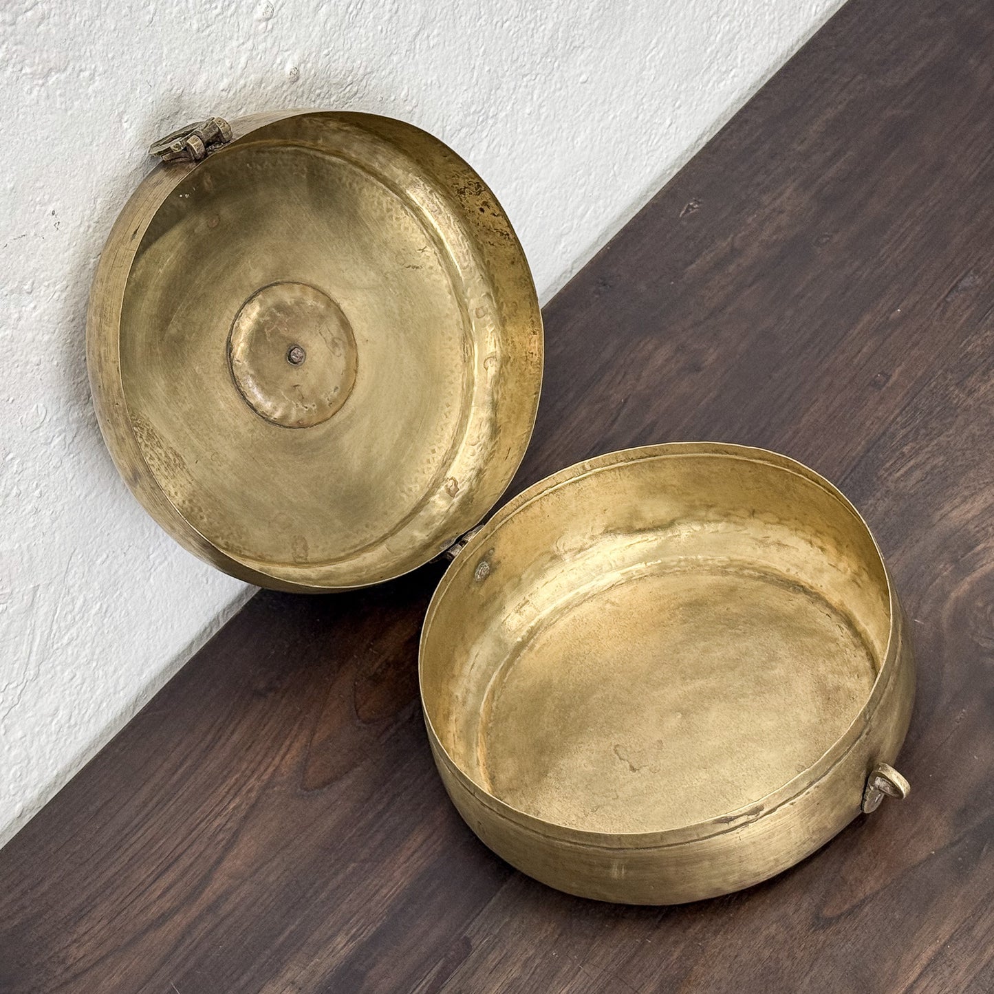 Two brass containers on a wooden surface with a white wall background