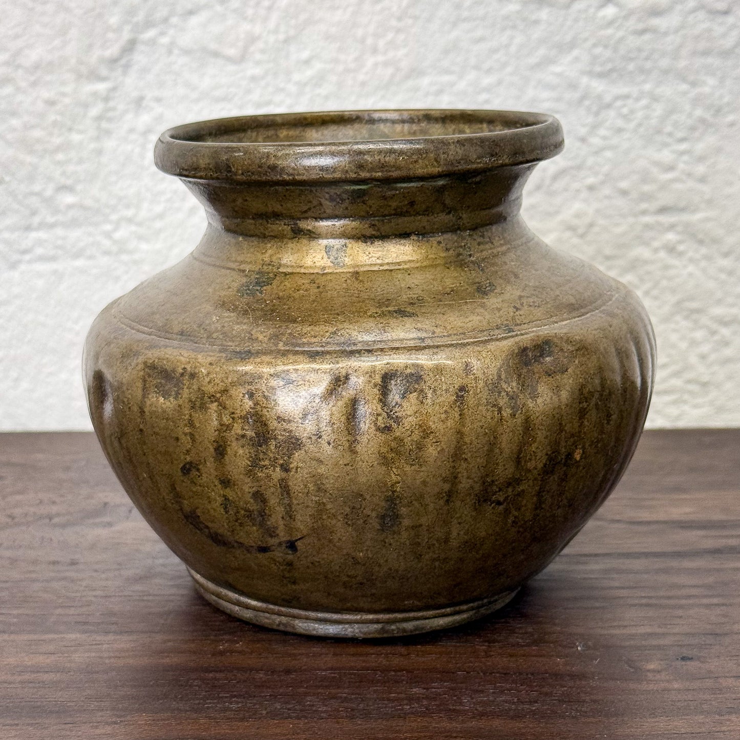 Bronze pot on a wooden surface with a textured white wall background