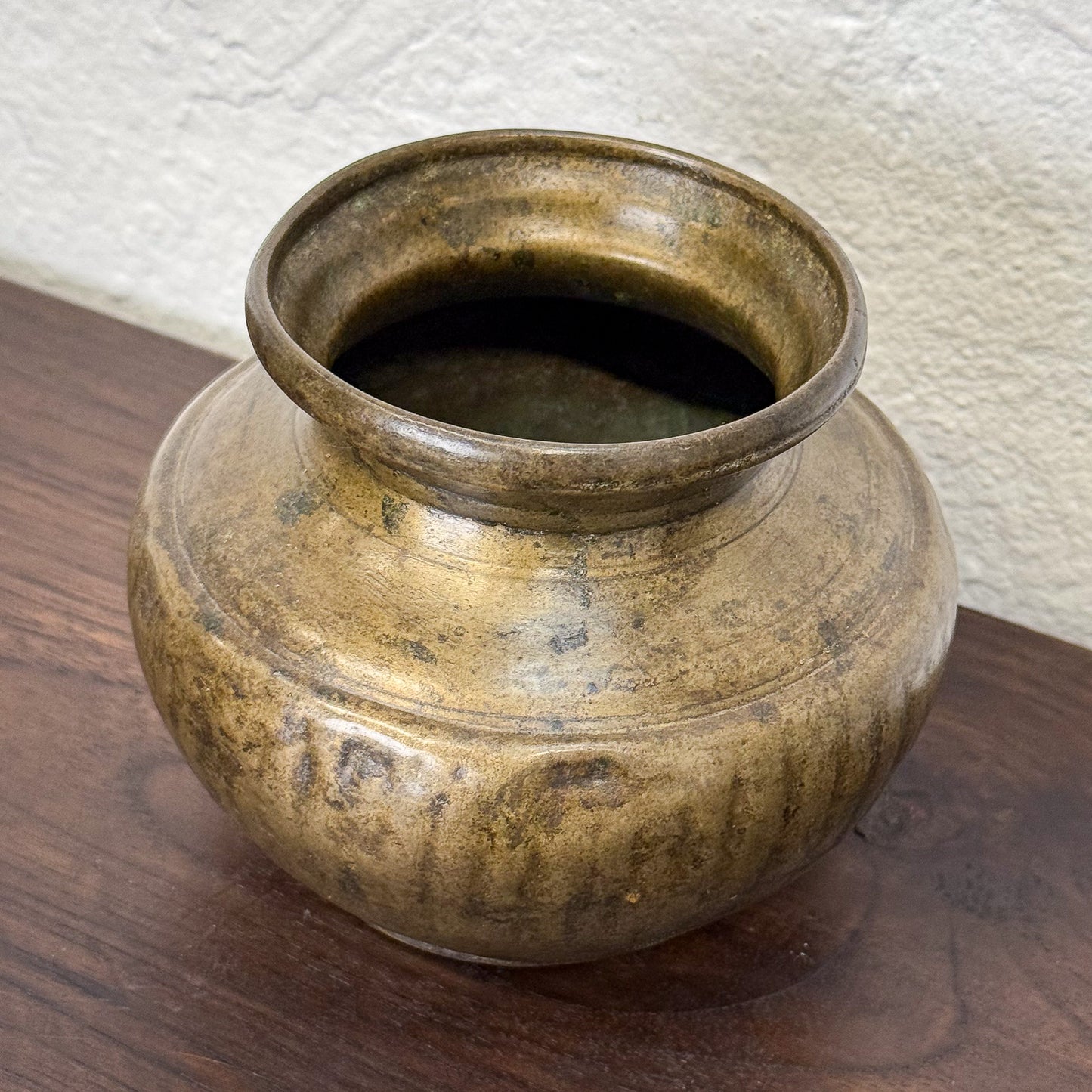 Bronze pot on a wooden surface with a textured white wall background