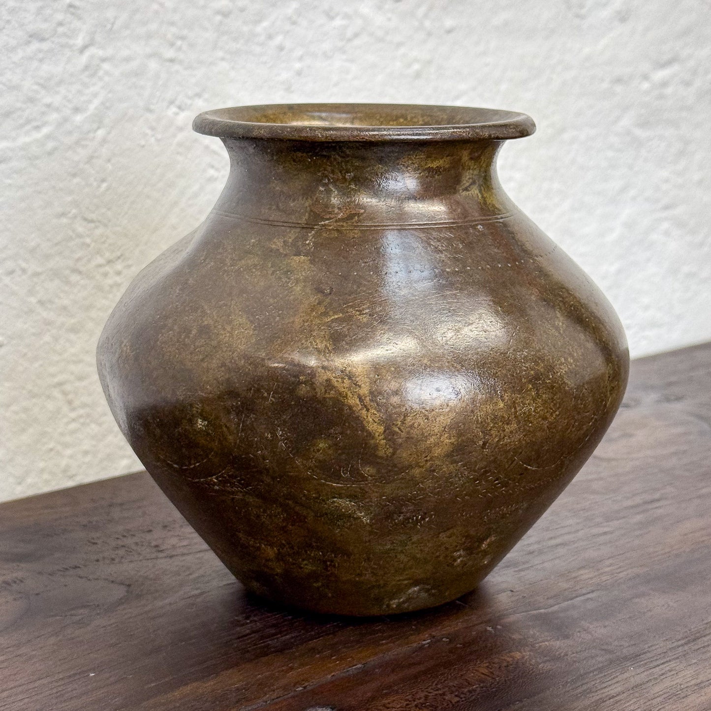 Brown ceramic vase on a wooden surface with a textured white wall background