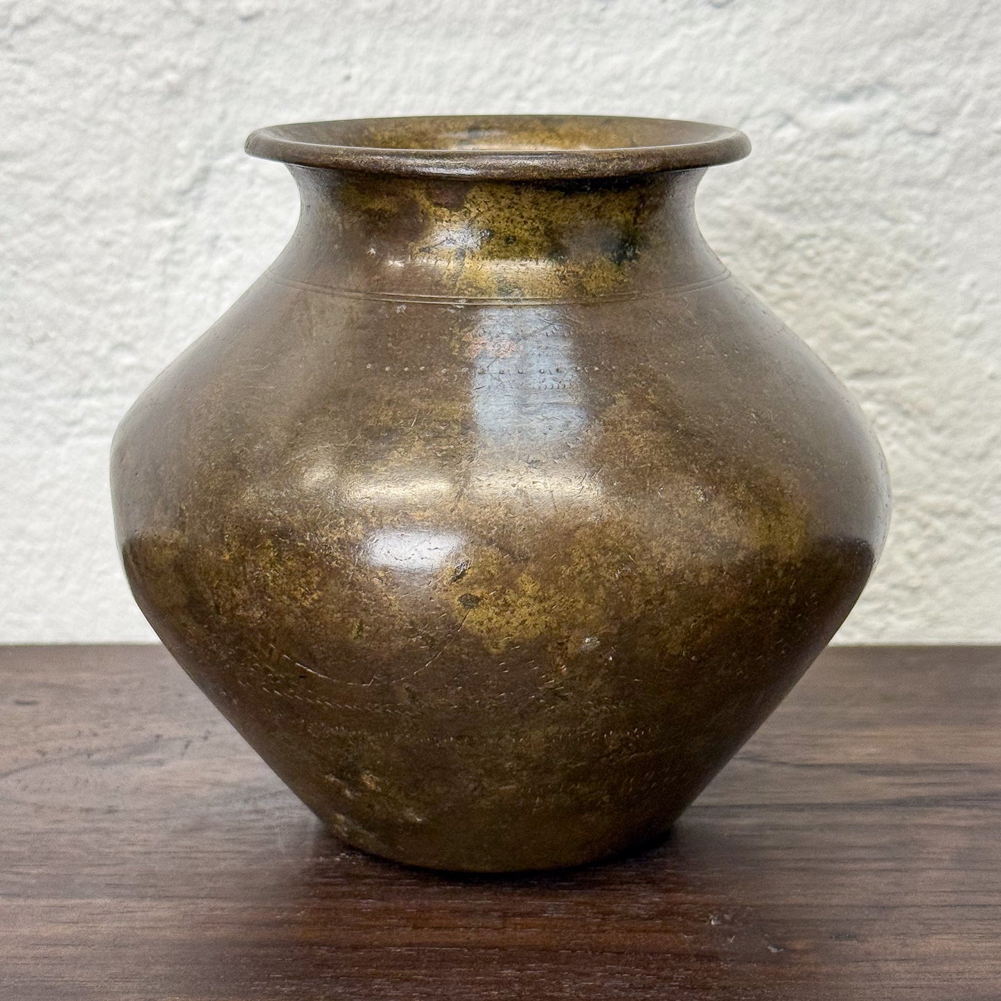 Bronze vase on a wooden surface with a textured white wall background