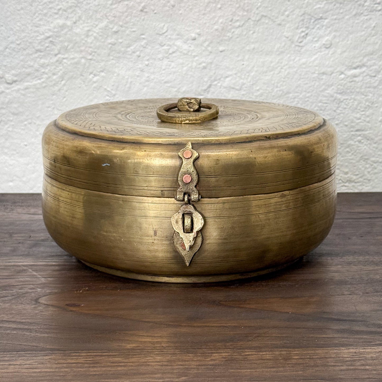 Brass decorative box with intricate designs on a wooden surface