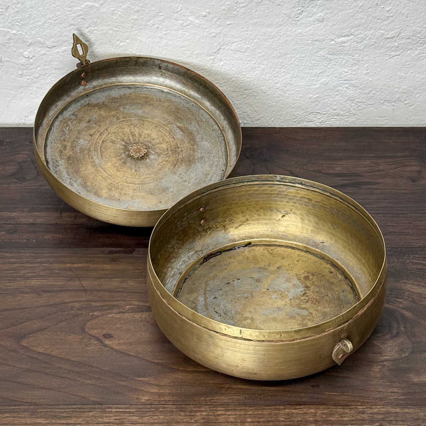Two brass trays on a wooden surface with a white textured wall background