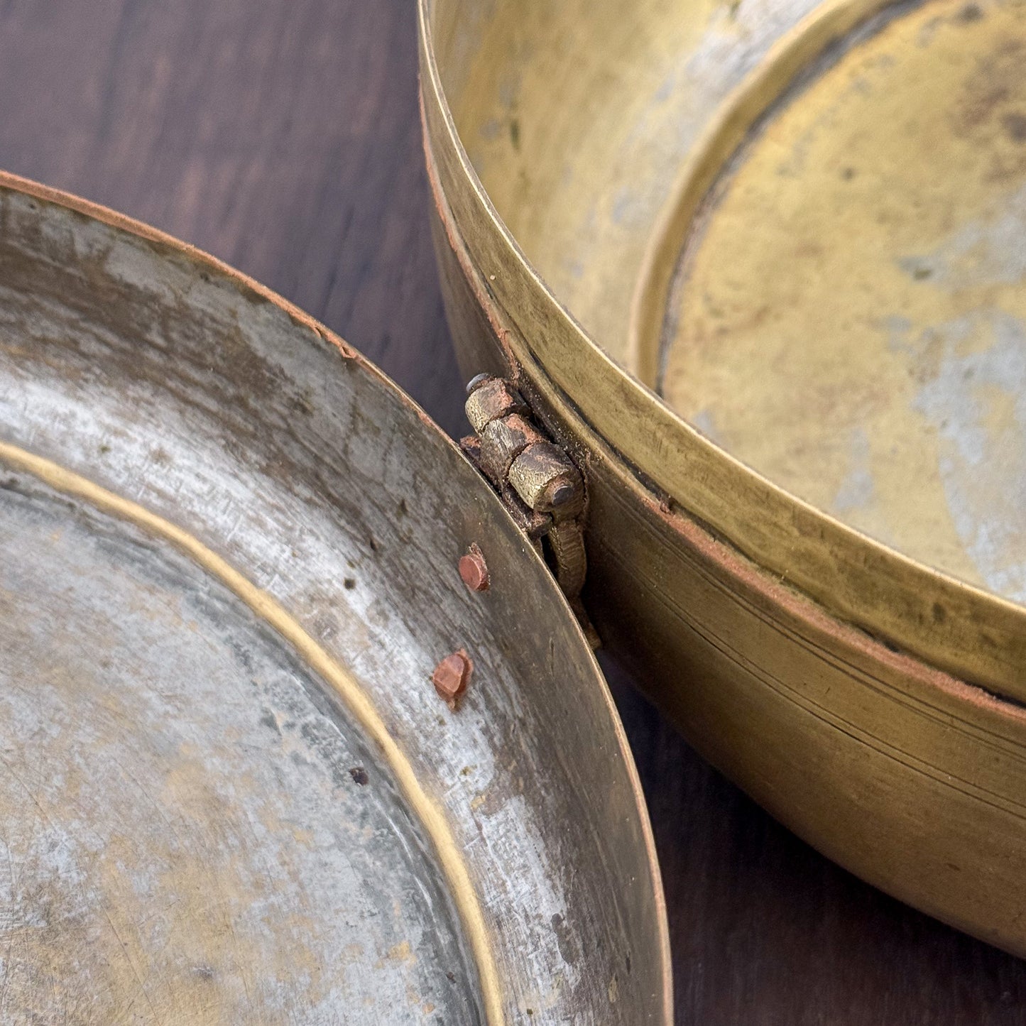 Close-up of two metallic bowls, one brass and one silver, on a wooden surface.