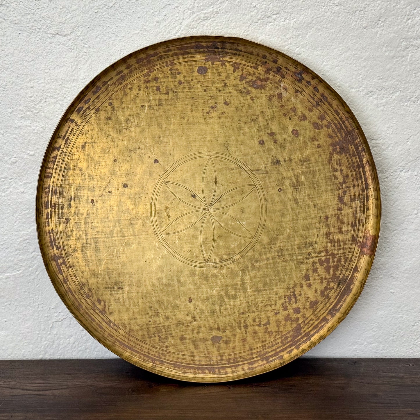 Round, gold-colored metal plate with engraved design on a white wall background