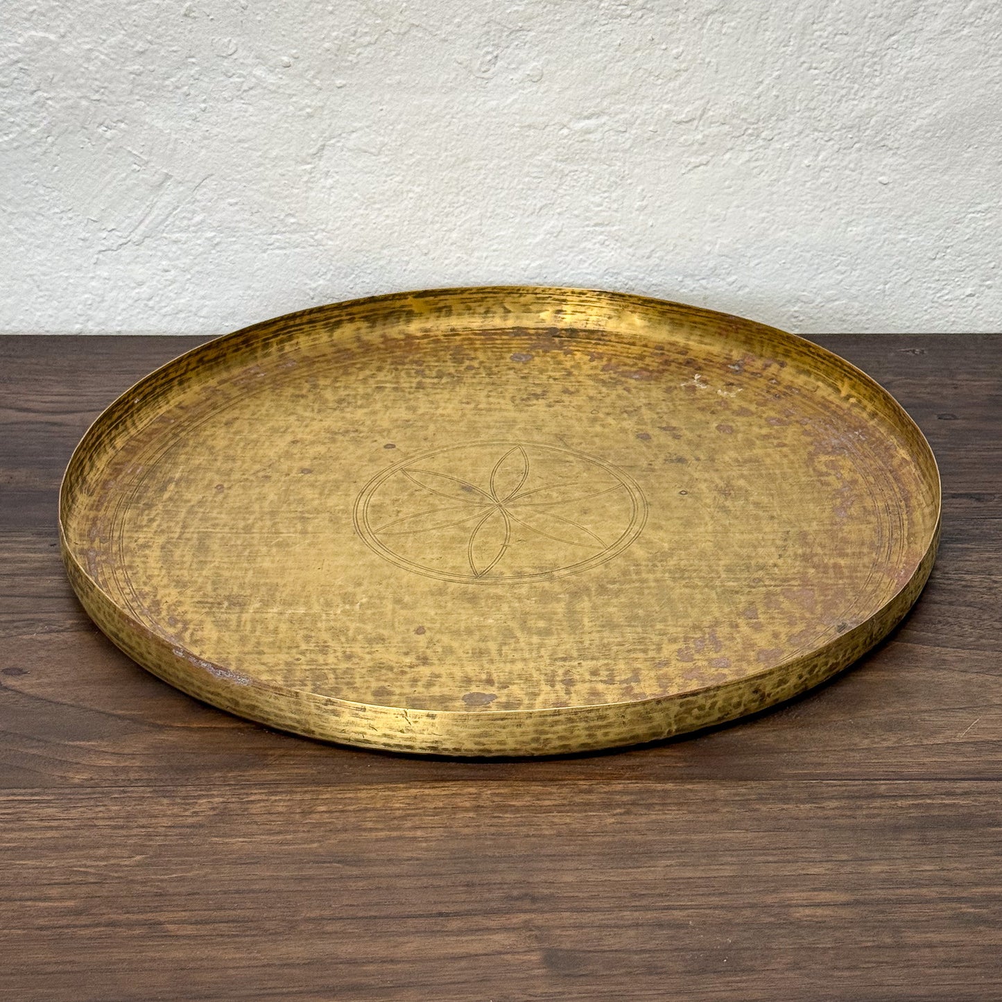 Gold decorative tray on a wooden surface with a white wall background