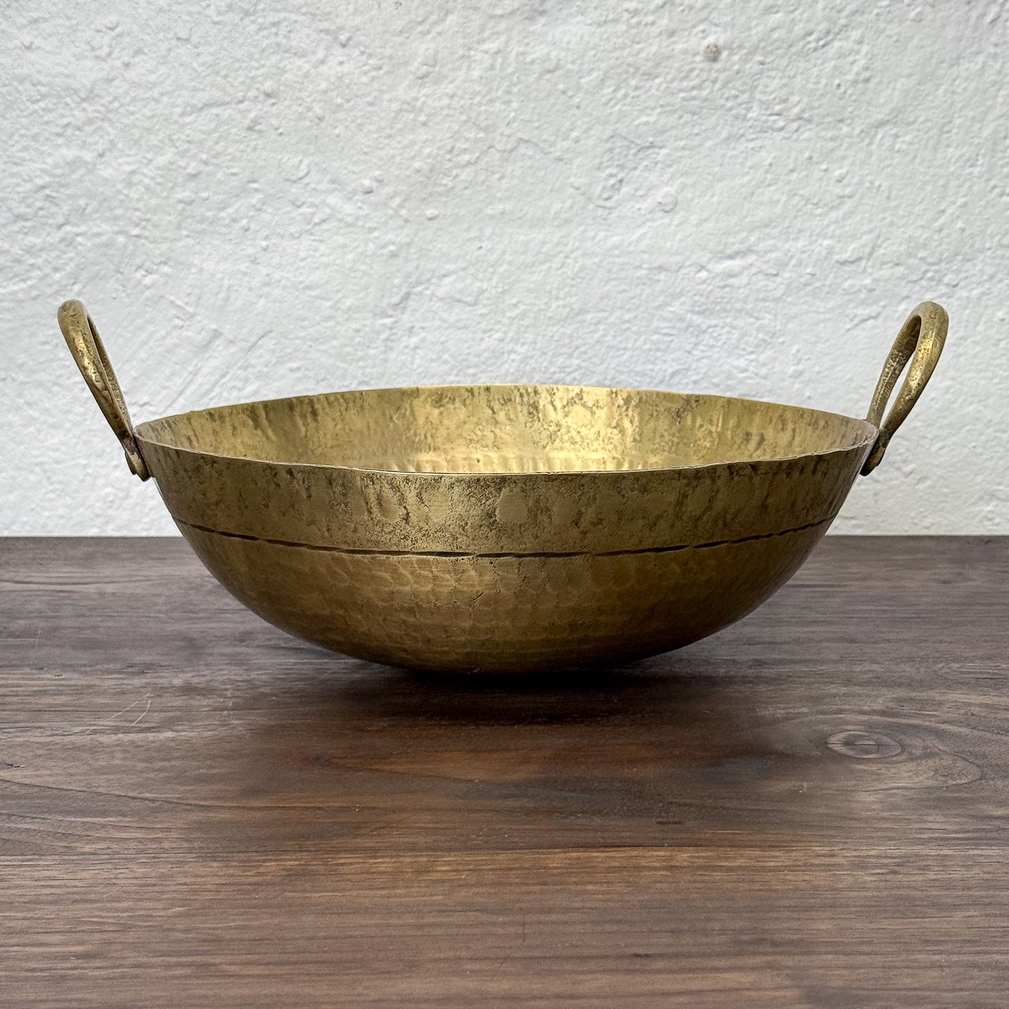 Brass bowl with handles on a wooden surface and white wall background