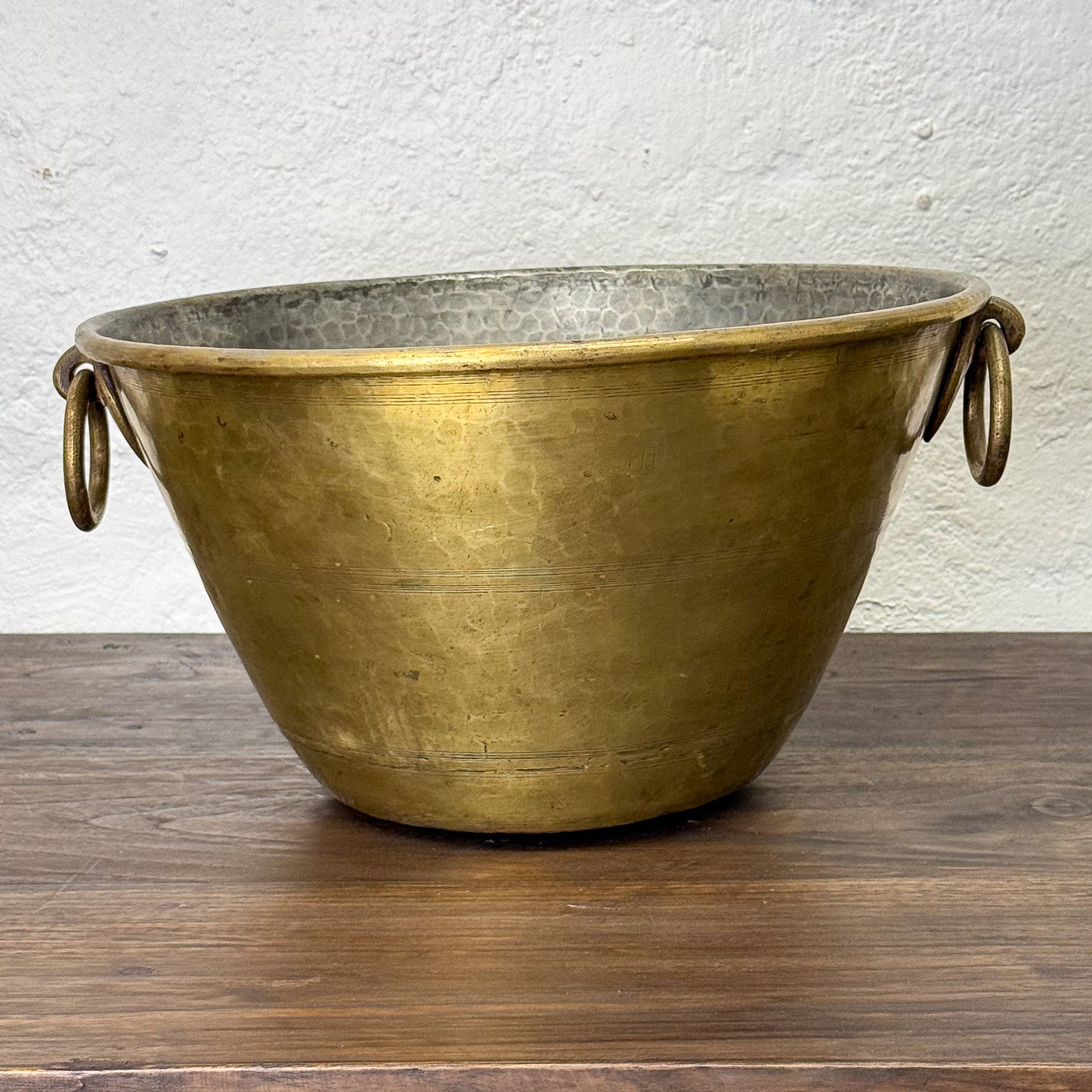 Brass planter with handles on a wooden surface and white wall background