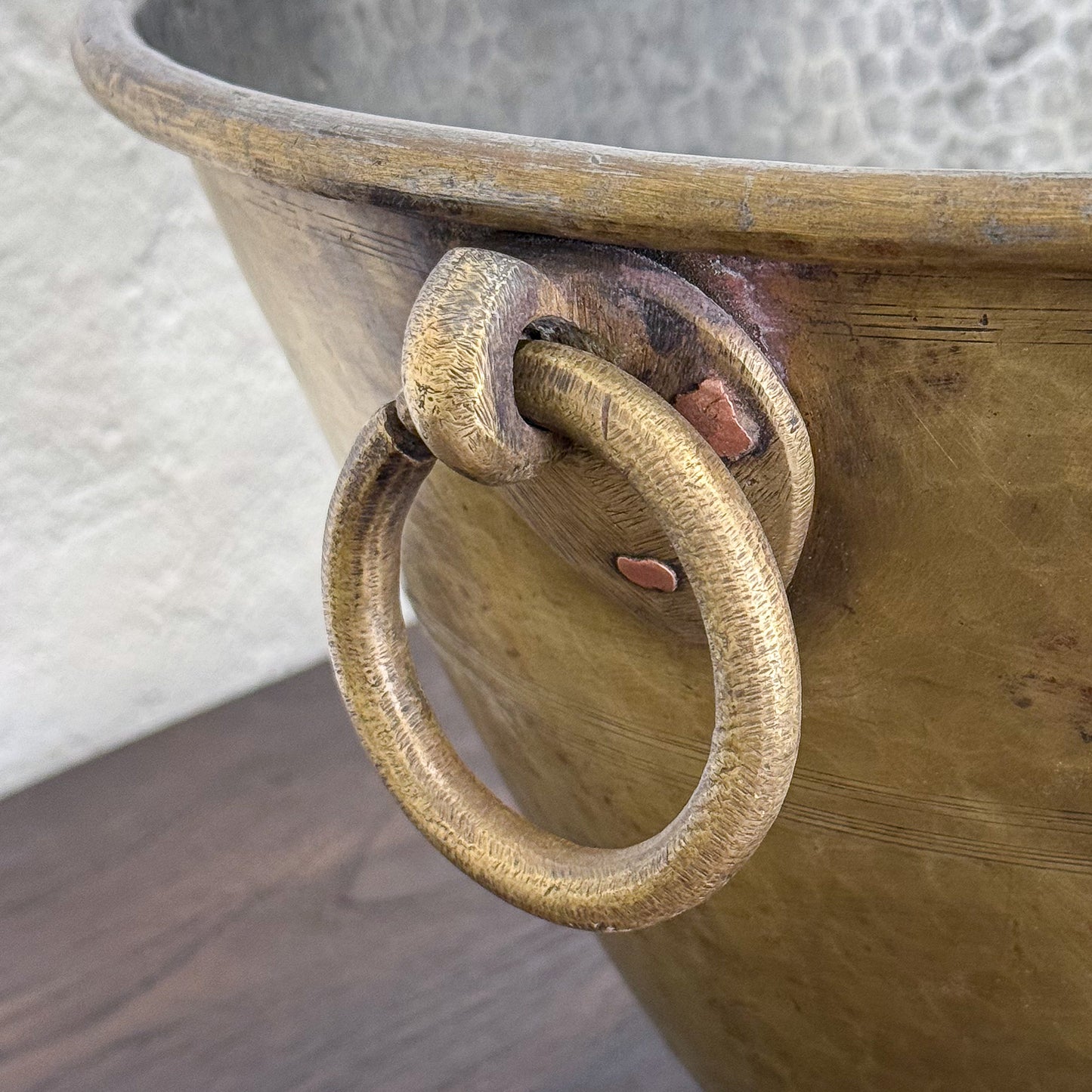 Close-up of a wooden bucket with a metal ring handle on a textured surface.