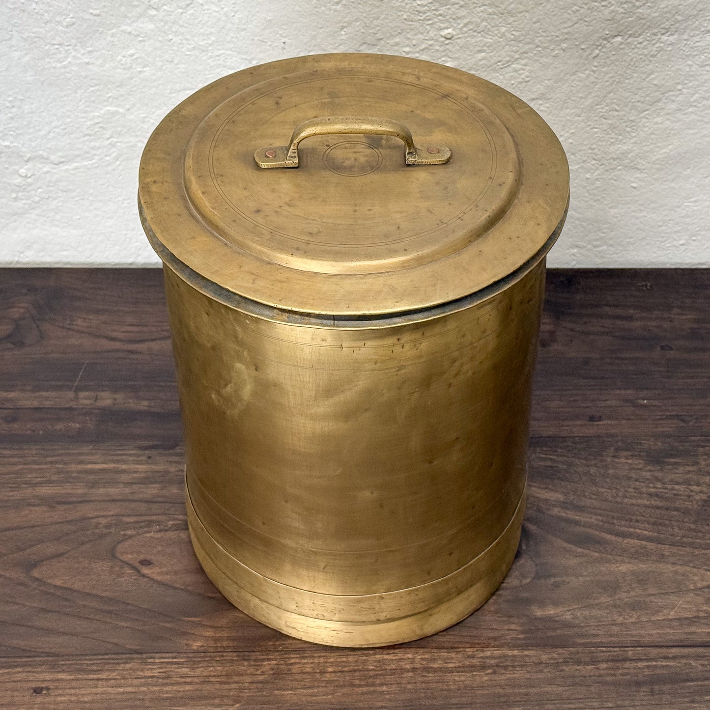 Brass cylindrical container with lid on a wooden floor