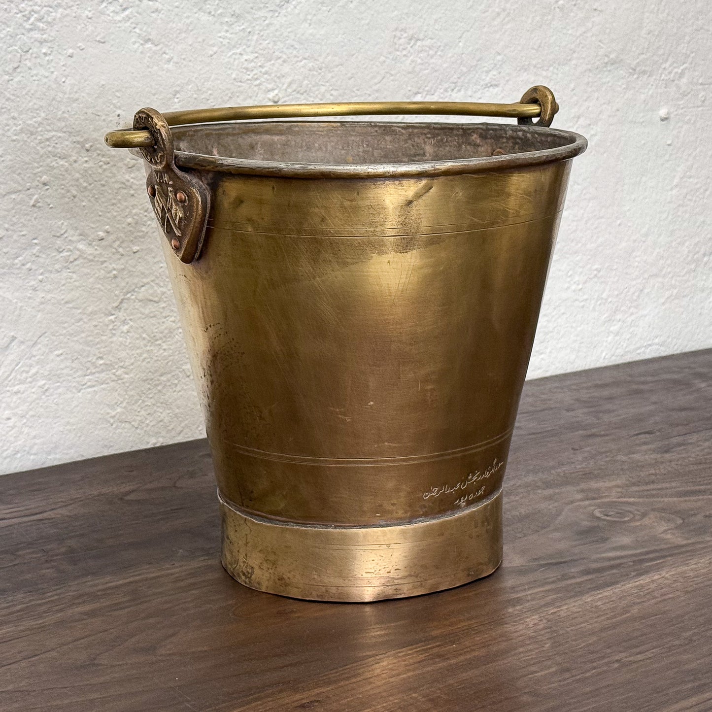 Brass bucket with a handle on a wooden surface against a white wall