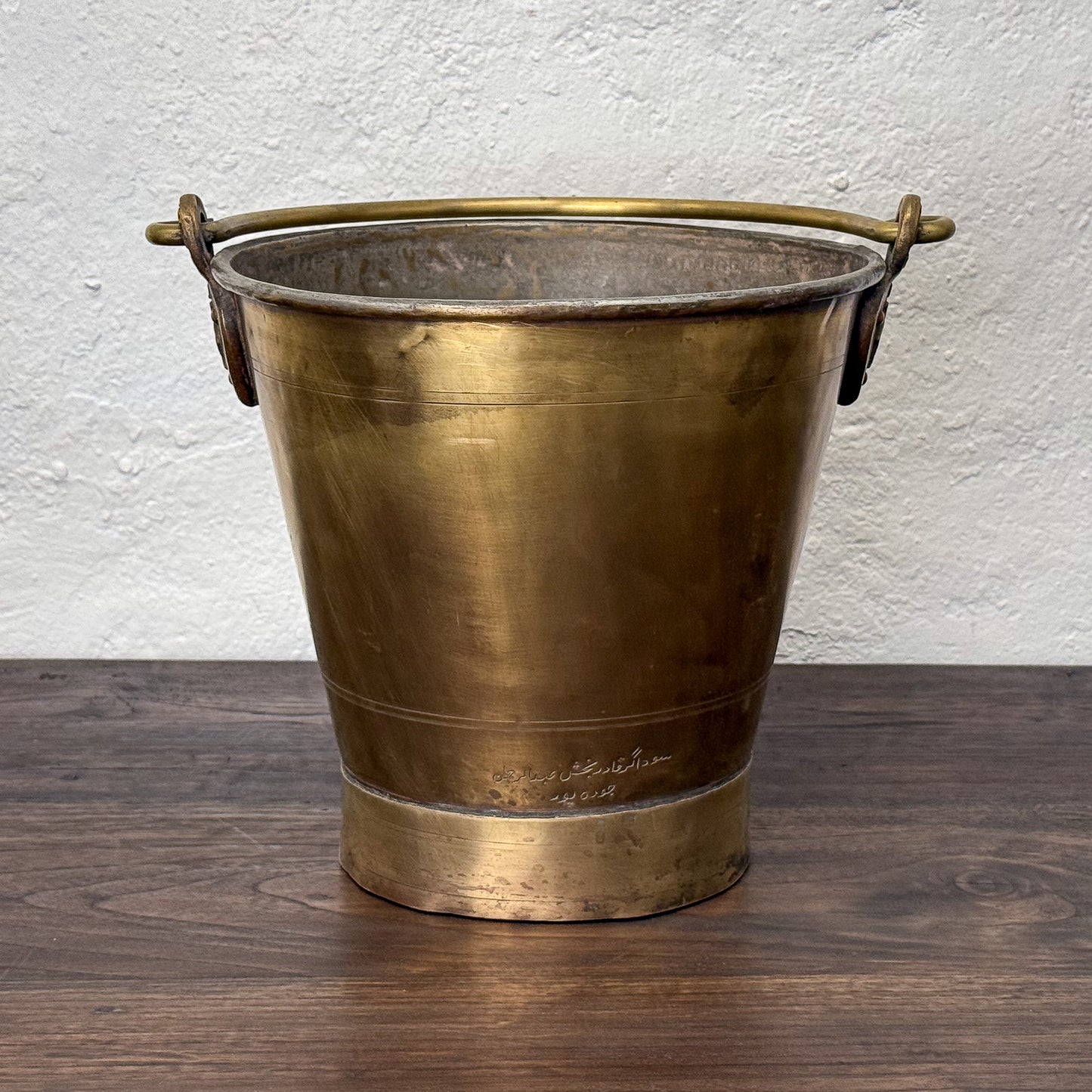 Bronze bucket with handles on a wooden surface and white wall background