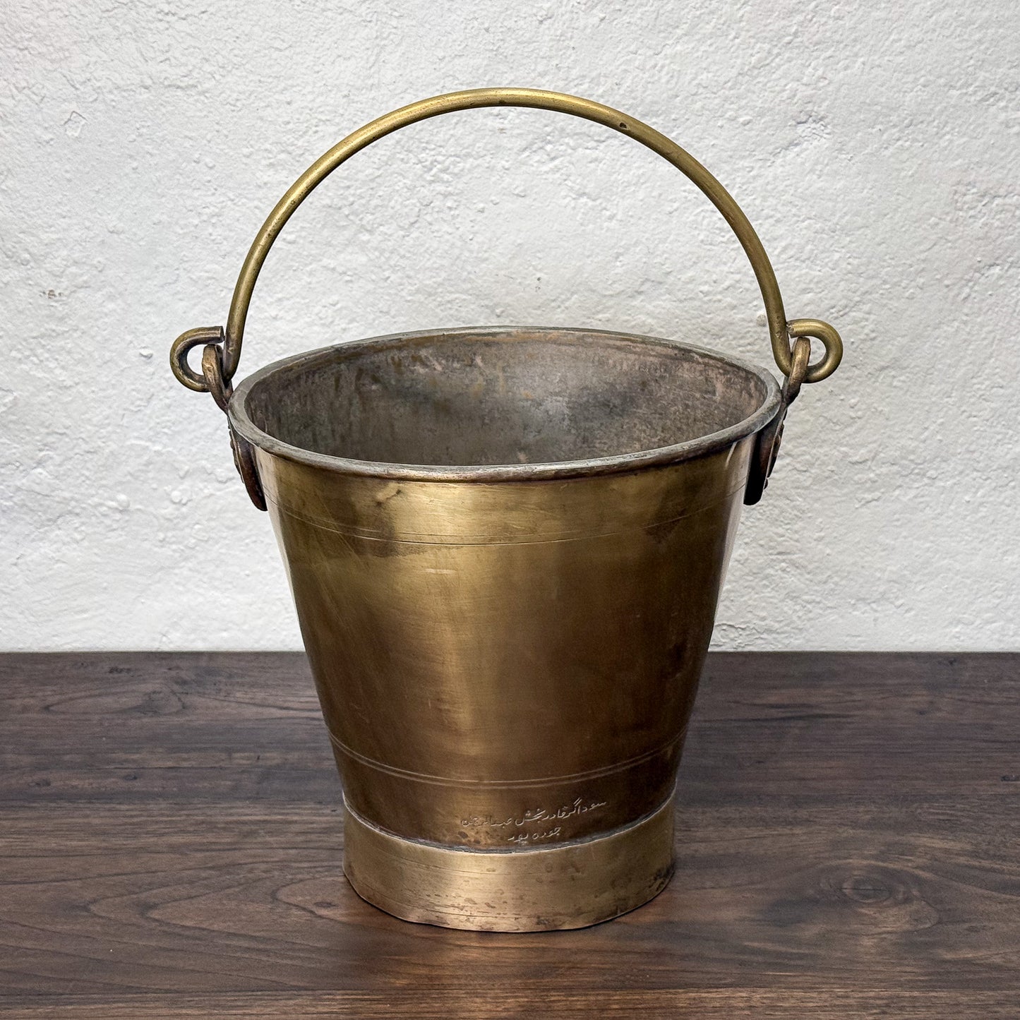 Bronze bucket with a handle on a wooden surface against a white wall