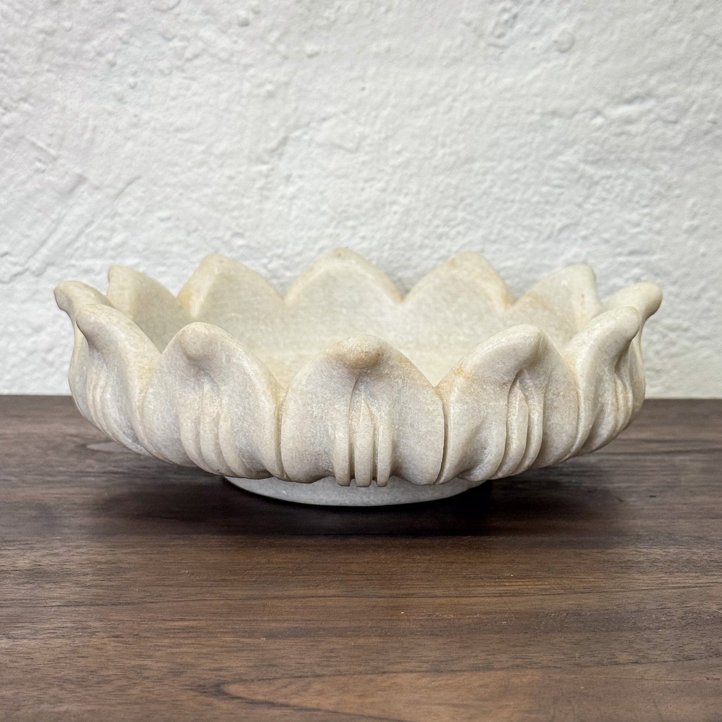 Decorative stone bowl with a lotus design on a wooden surface and white textured wall background