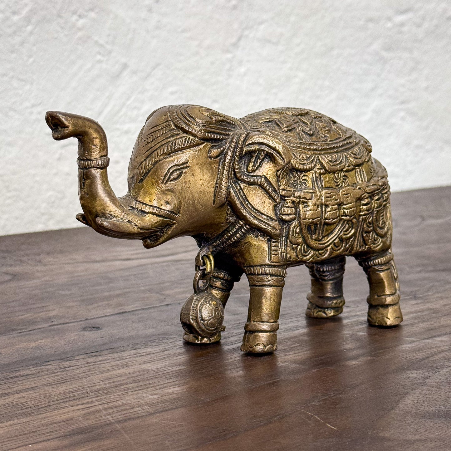 Decorative brass elephant figurine on a wooden surface with a white textured wall background