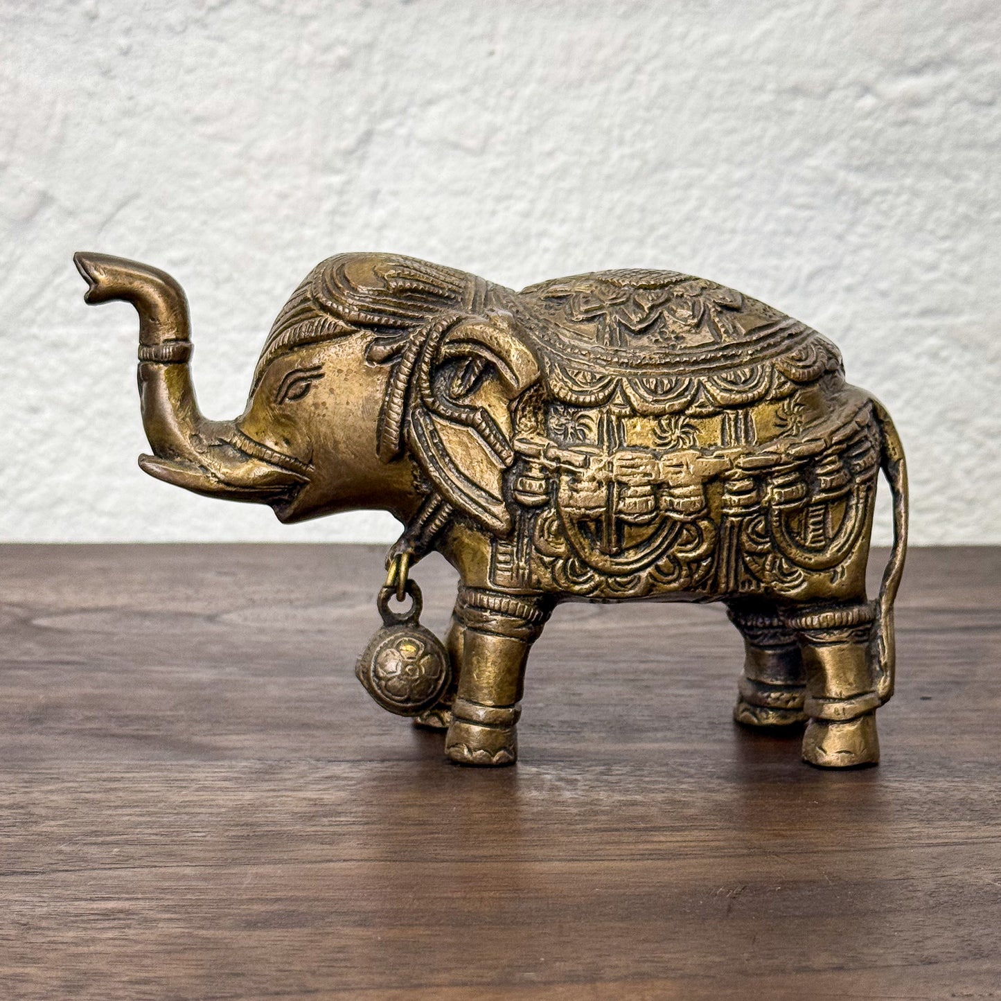 Decorative brass elephant figurine on a wooden surface with a white textured wall background
