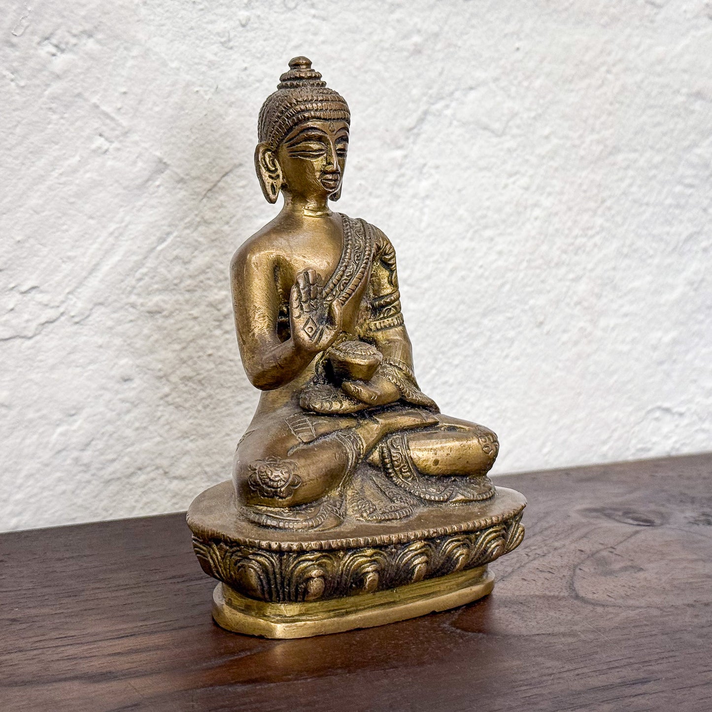 Bronze Buddha statue on a wooden surface with a textured white wall background
