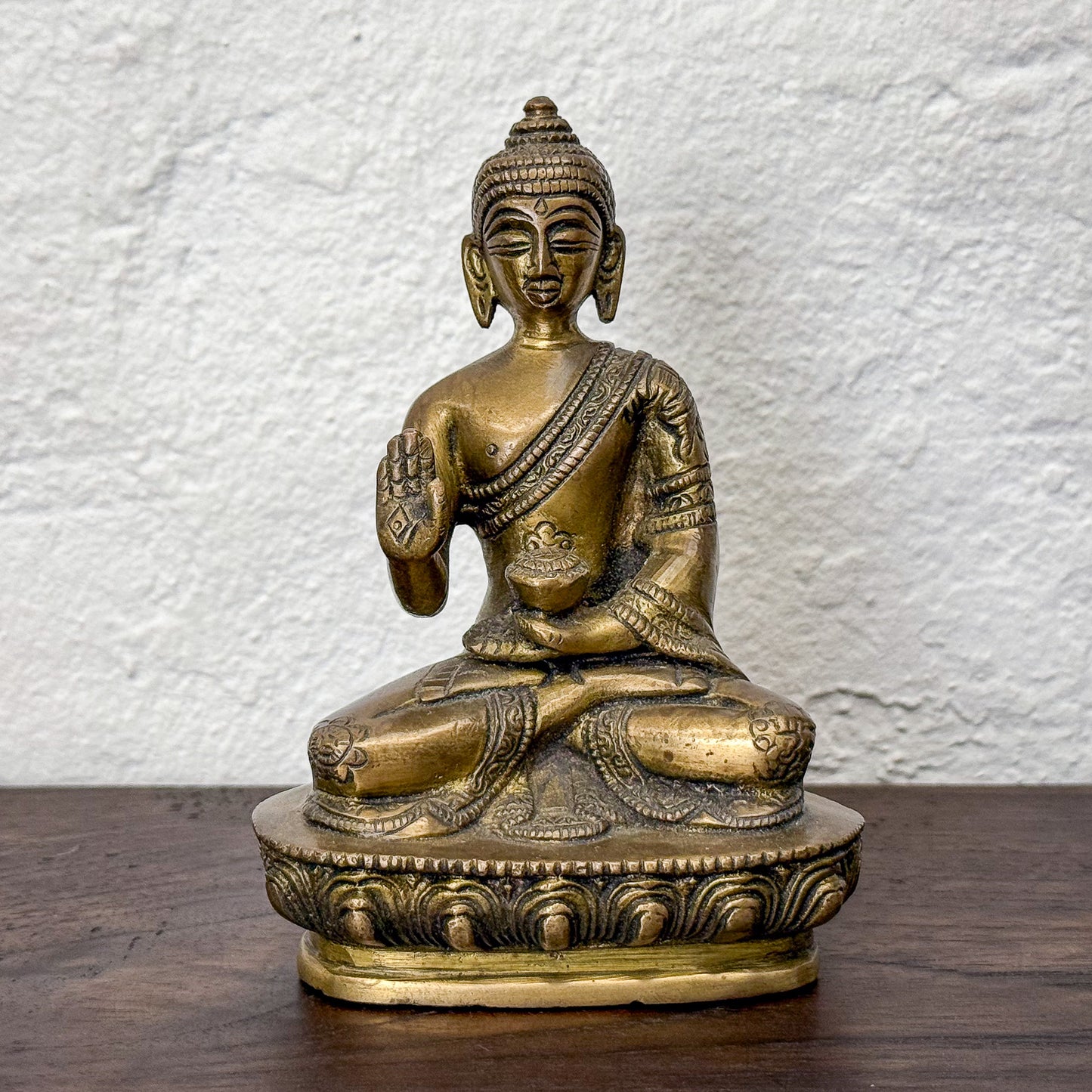 Bronze statue of a seated figure on a wooden surface with a white textured wall background