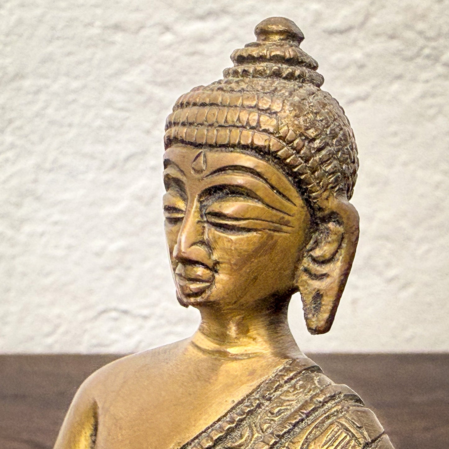 Bronze statue of a seated figure with intricate details against a textured white wall.