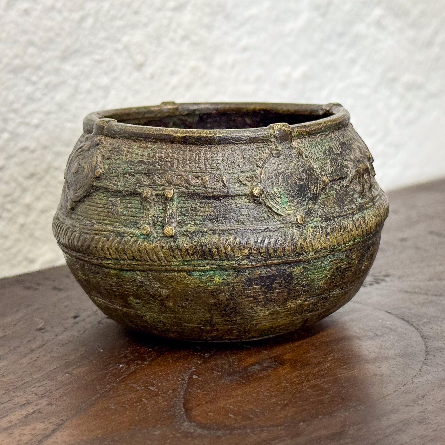 Ancient bronze bowl with intricate designs on a wooden surface