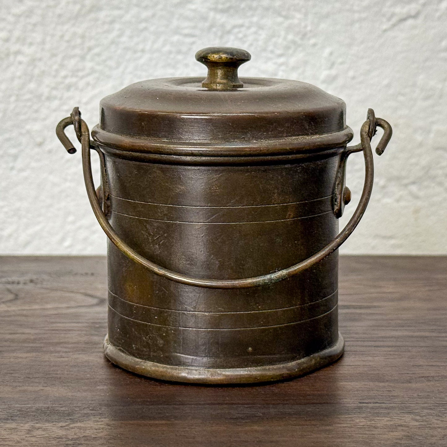 Bronze metal canister with lid on a wooden surface