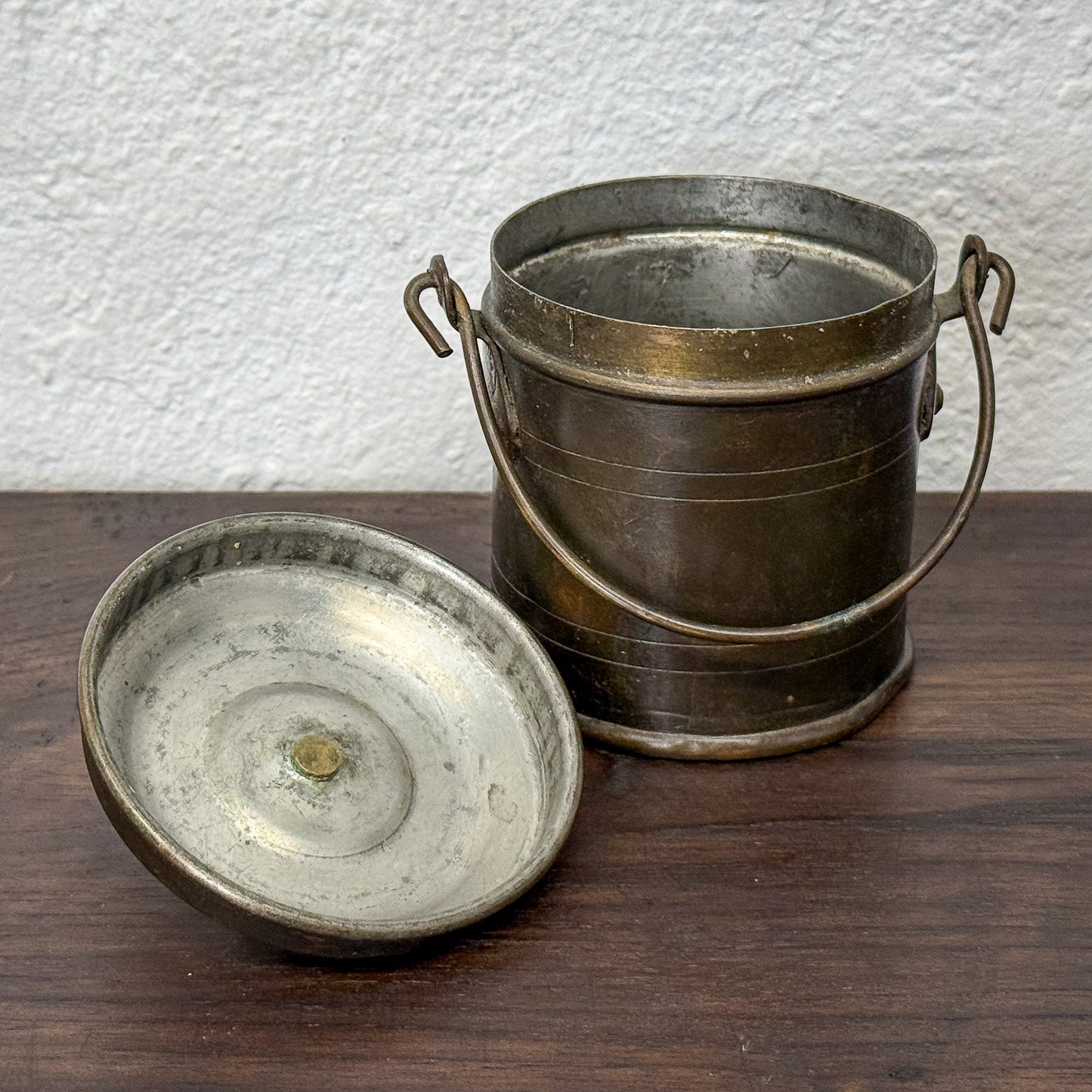 Vintage metal bucket and lid on a wooden surface with a white wall background