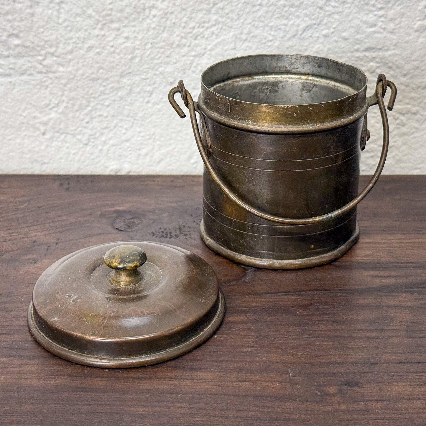Bronze bucket with handles and cover on a wooden surface