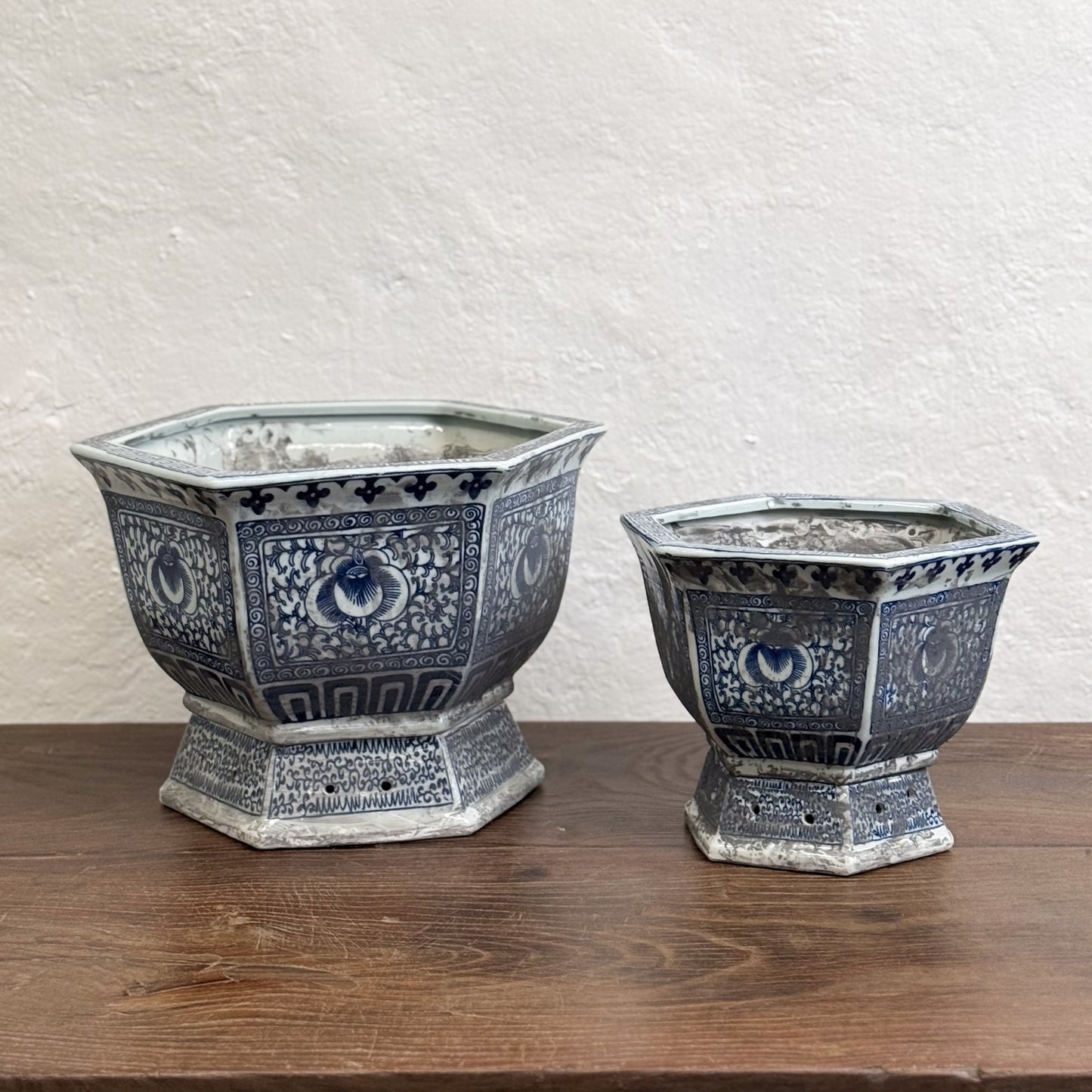 Two hexagonal porcelain planters with blue floral patterns on a wooden surface against a neutral background.