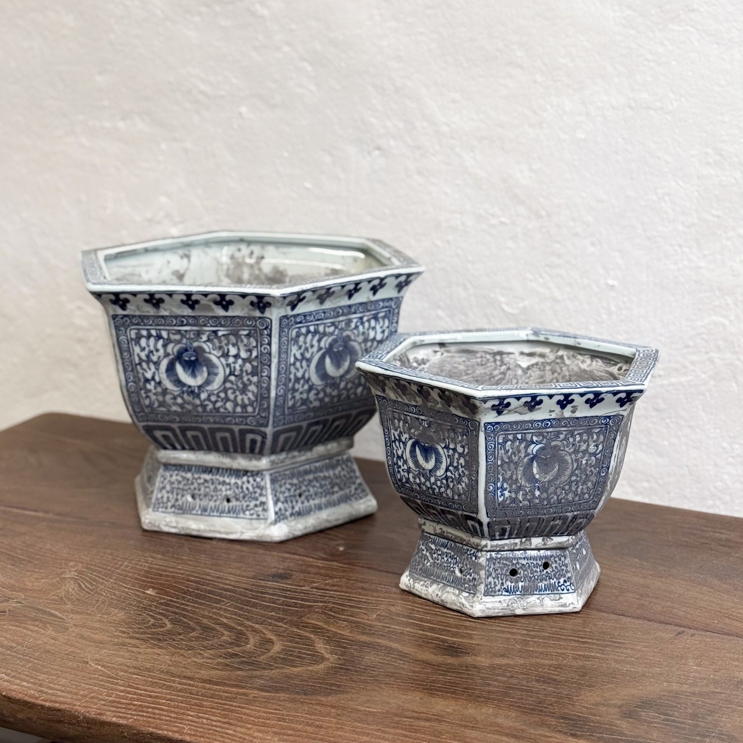 Two hexagonal porcelain planters with blue floral patterns on a wooden surface against a neutral background.
