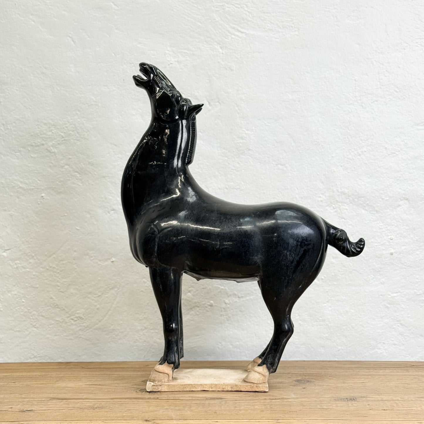 Black horse sculpture on a wooden base against a white textured wall