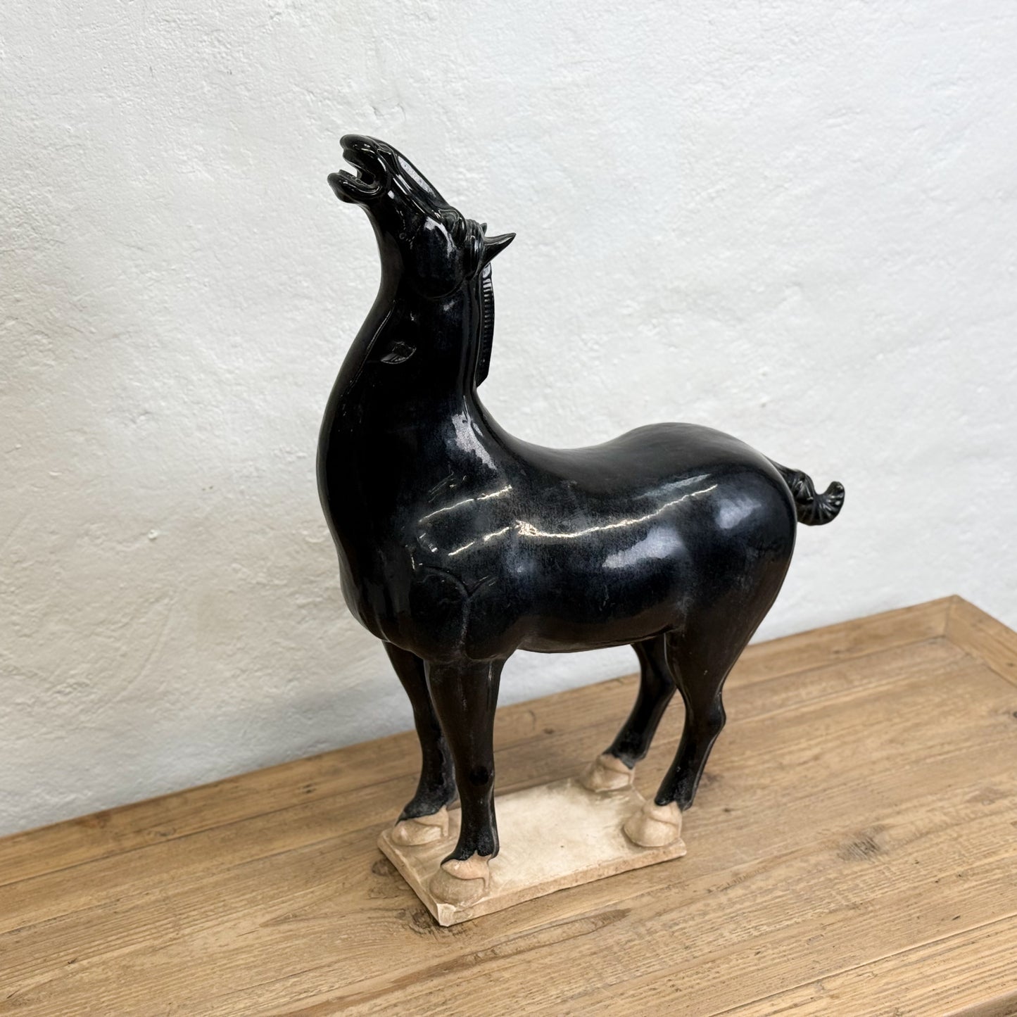 Black marble sculpture of a horse on a wooden base against a white wall.