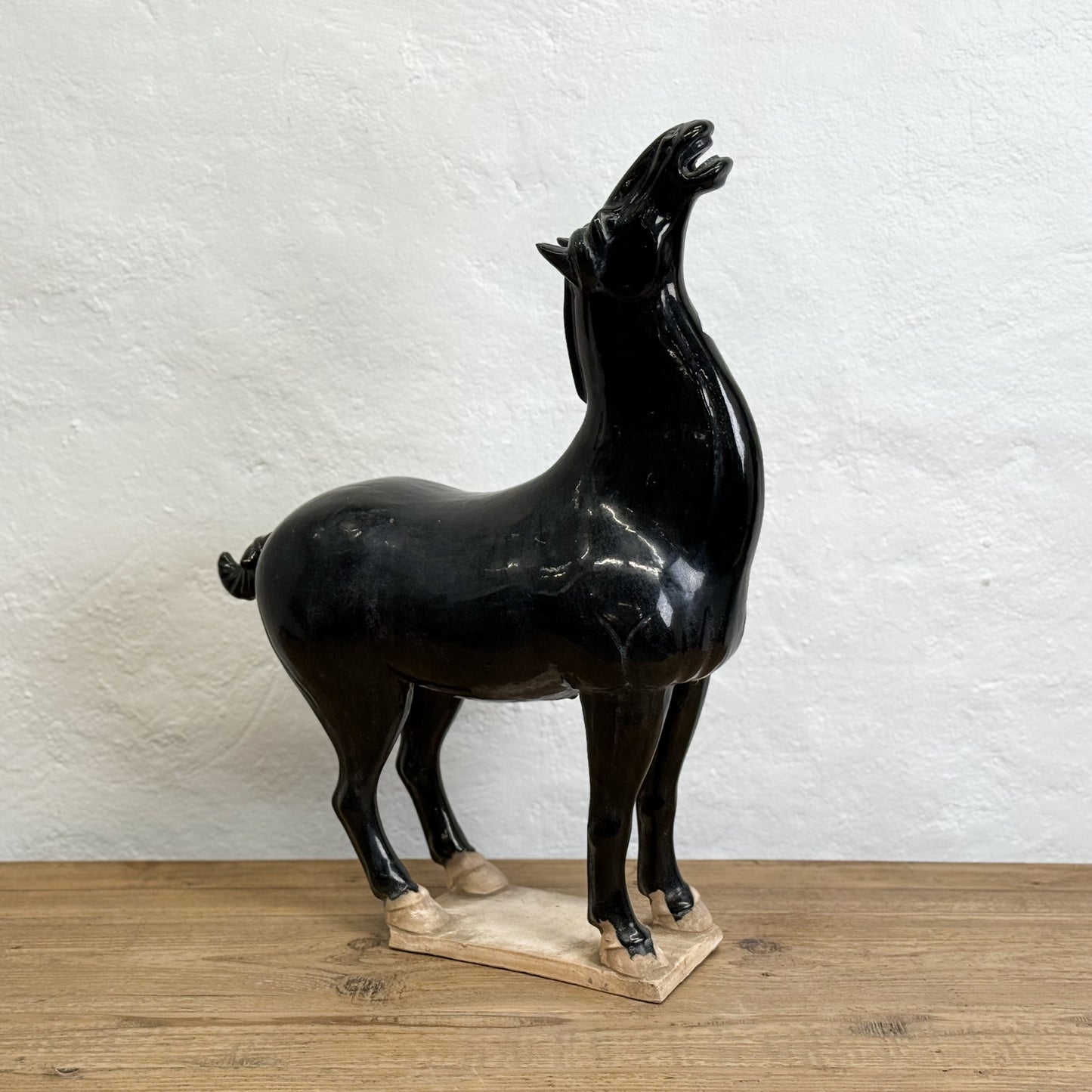 Black ceramic horse sculpture on a wooden base against a white wall